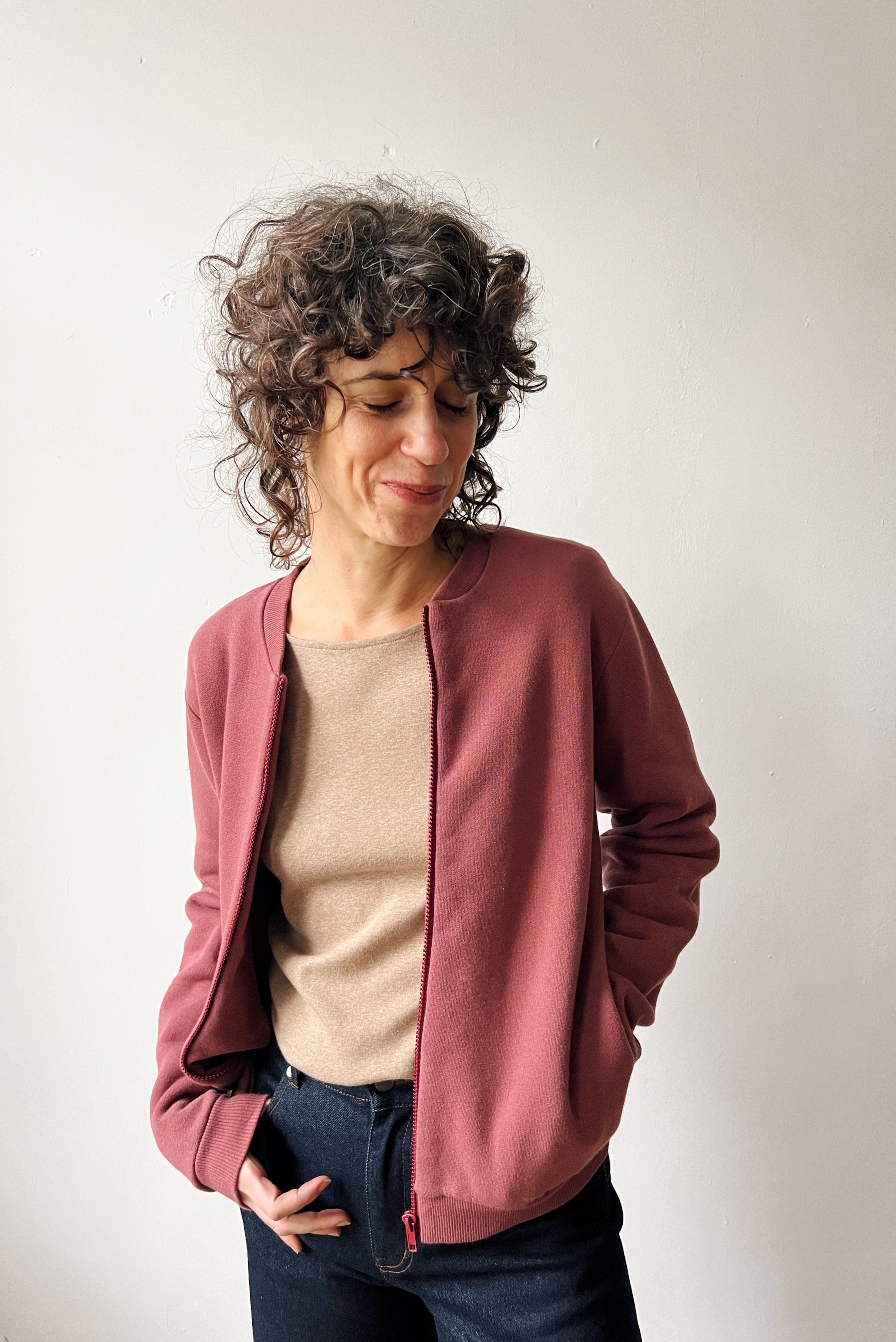 Woman wearing a figue bomber over a beige top and blue jeans against a white background