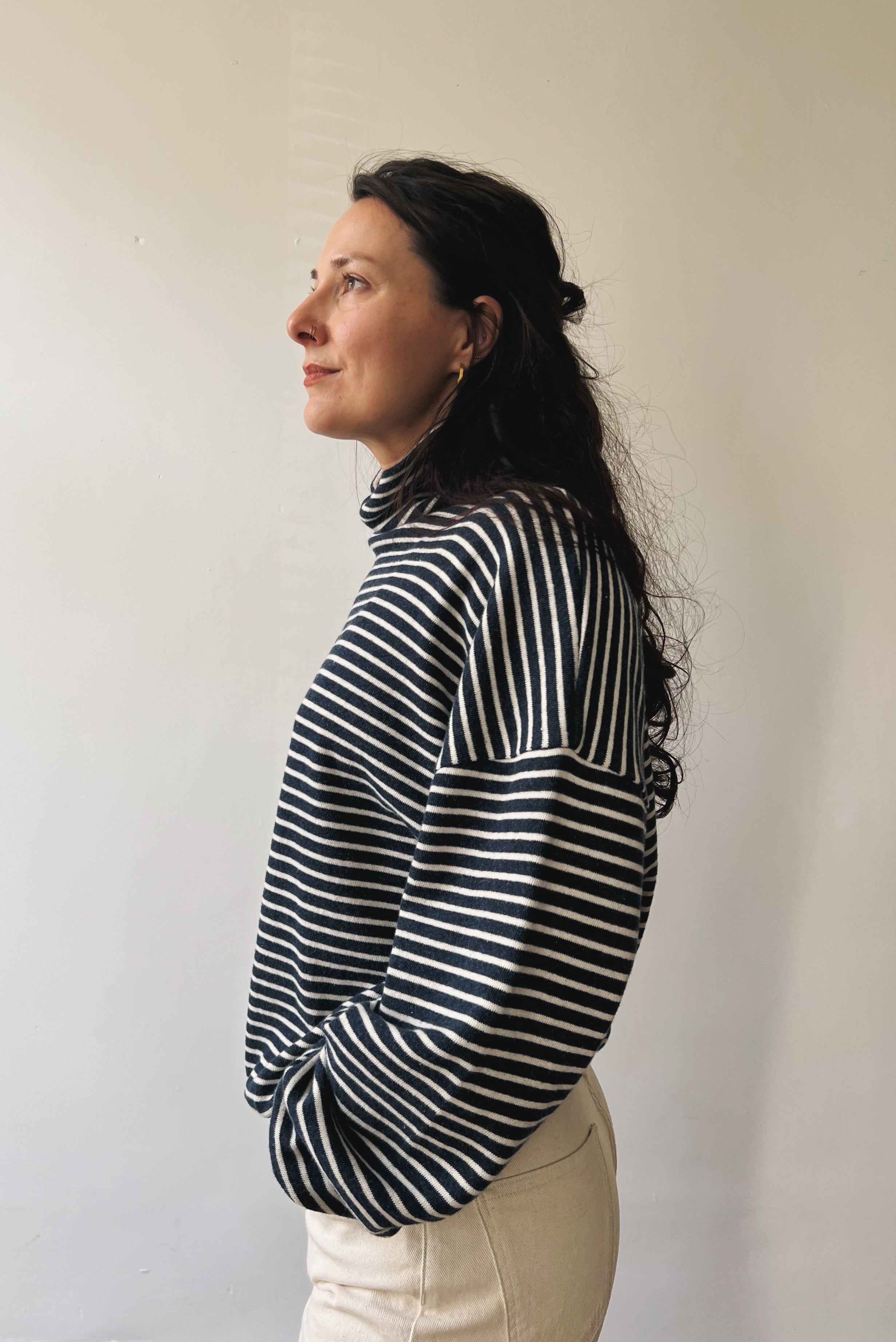 Woman wearing a blue and white striped sweater with turtleneck against a plain background