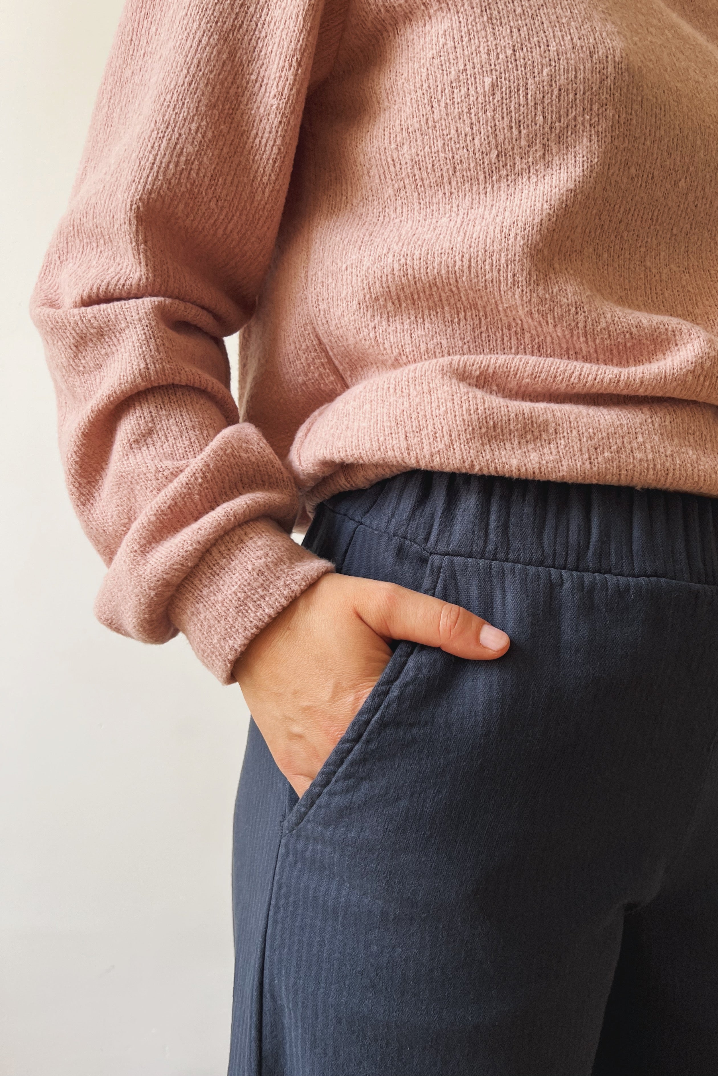 Woman wearing a pink sweater and dark blue pants with her hands in the pocket