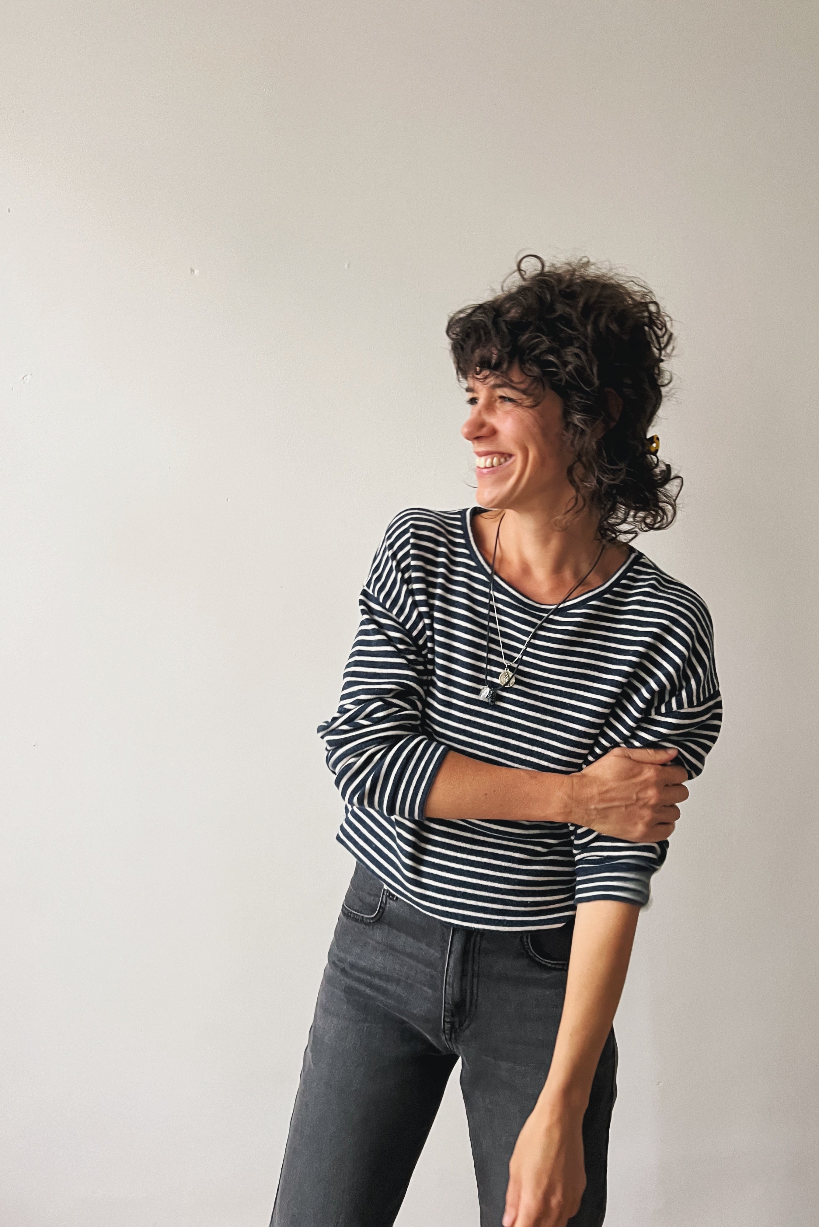 Woman wearing a blue and white striped sweater and gray jeans against a plain background
