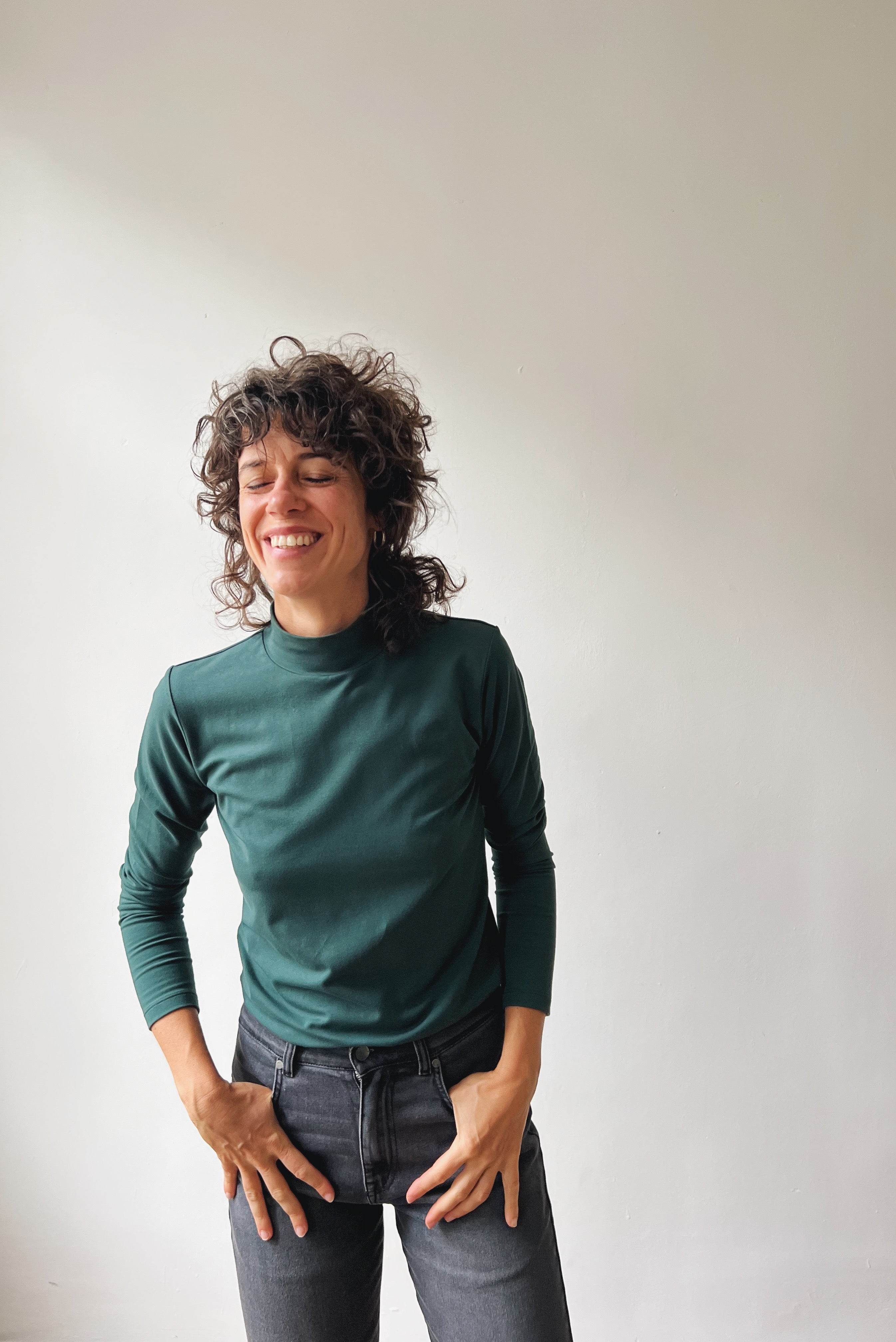Person wearing a pine turtleneck sweater and gray pants against a plain background