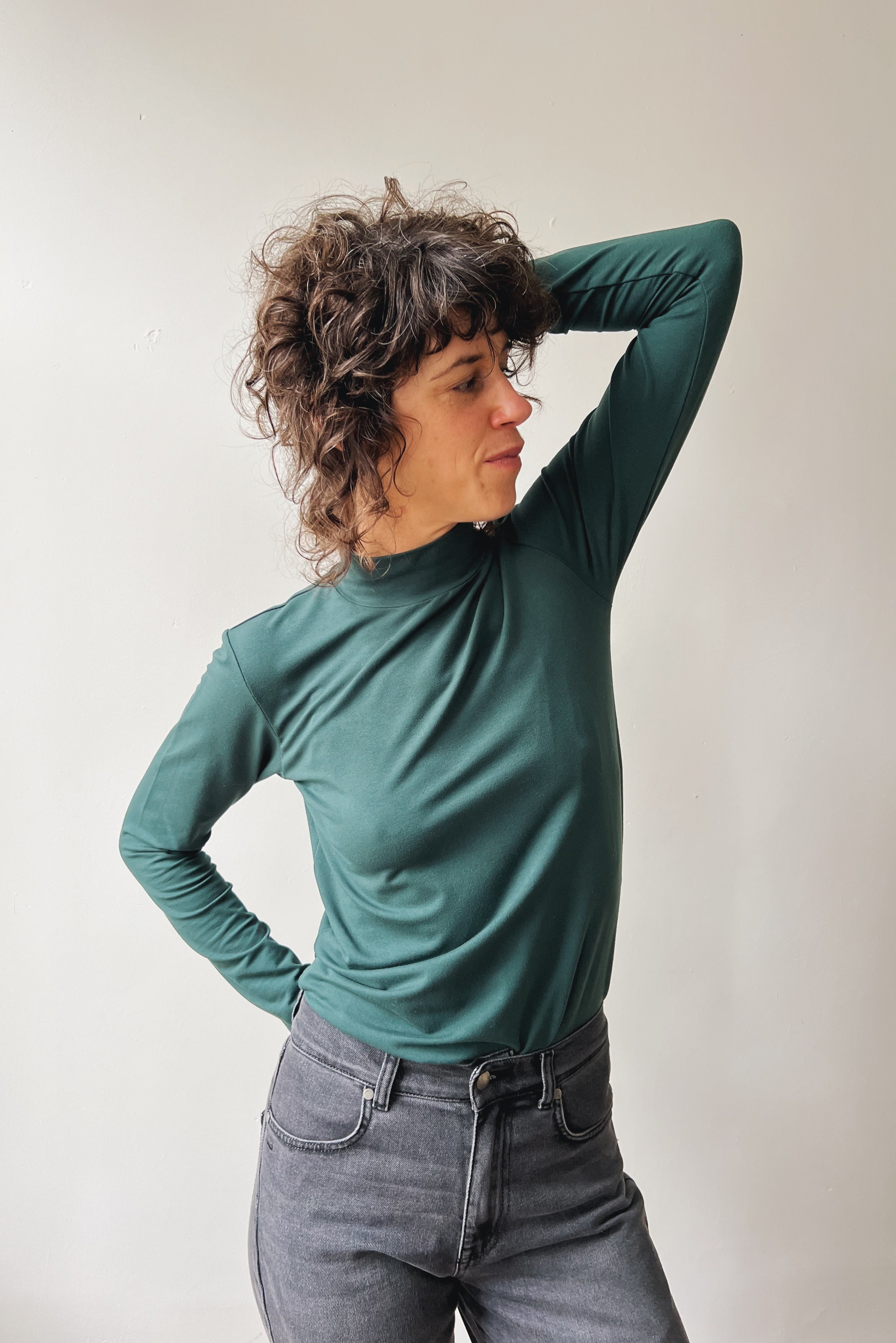 Person wearing a pine turtleneck sweater and gray pants against a plain background