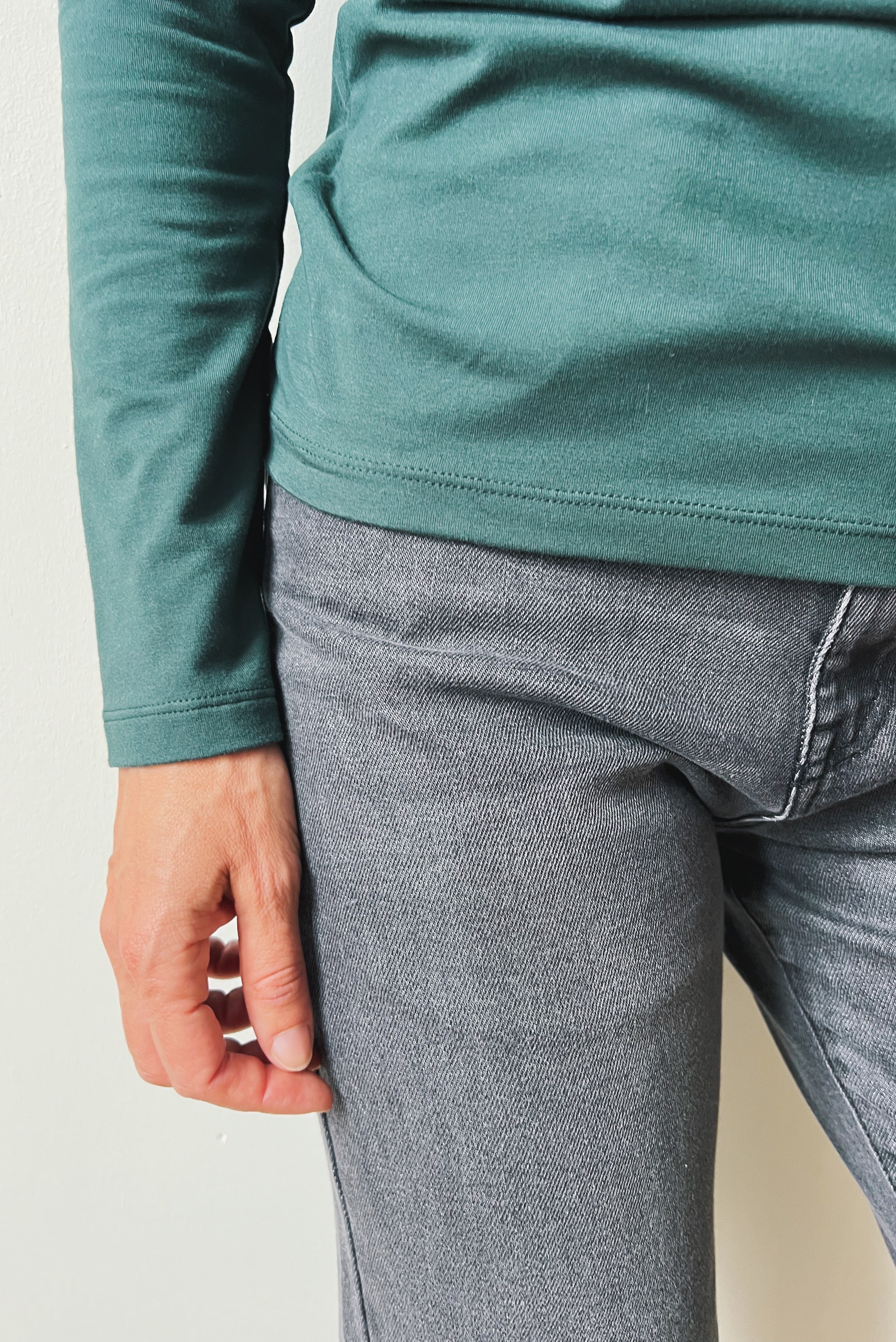 Person wearing a teal long-sleeve shirt and gray jeans against a neutral background