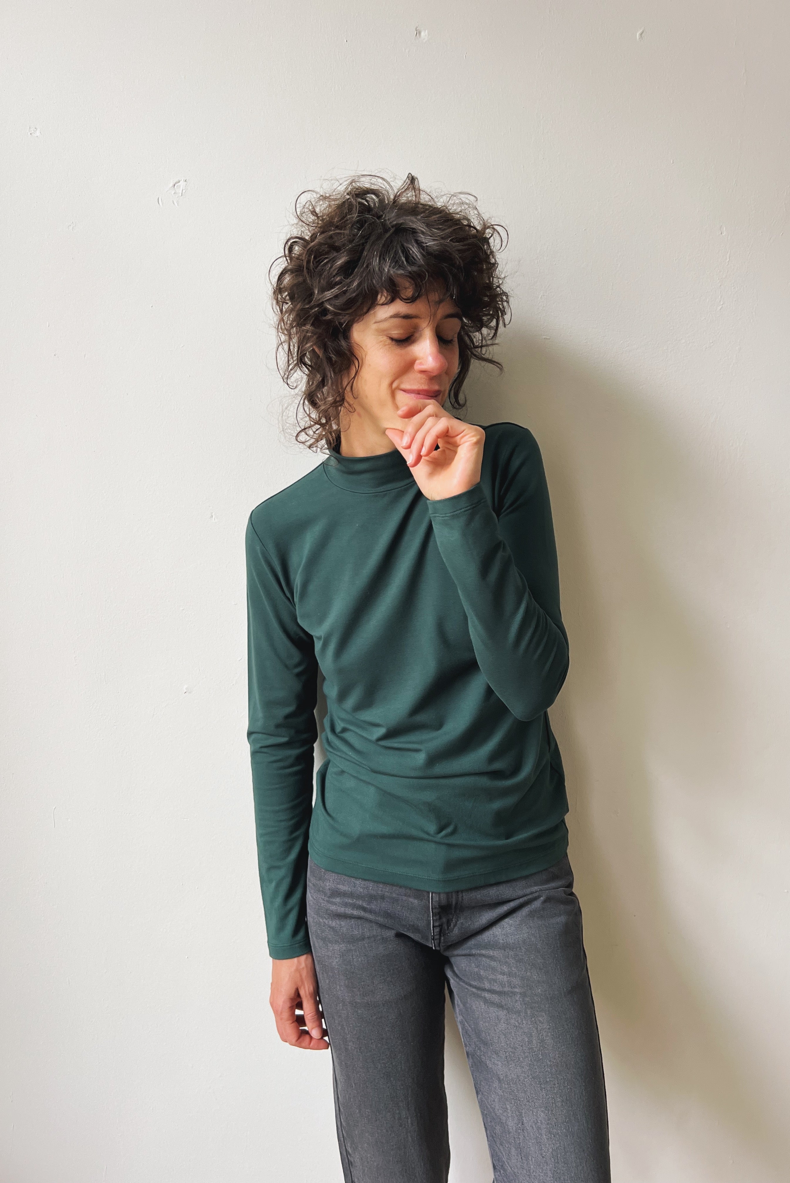 Person wearing a pine turtleneck sweater and gray pants against a plain background