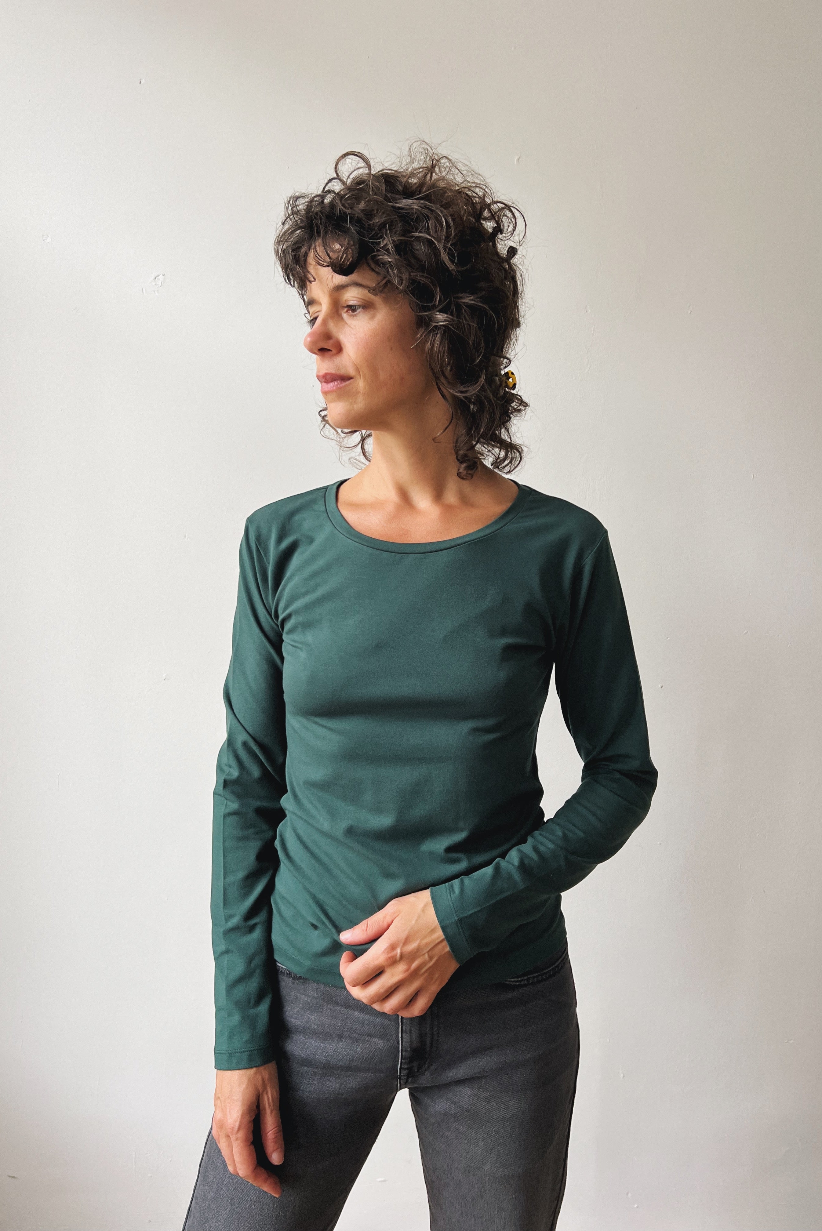 Woman wearing a pine long-sleeve and grey jeans against a plain background