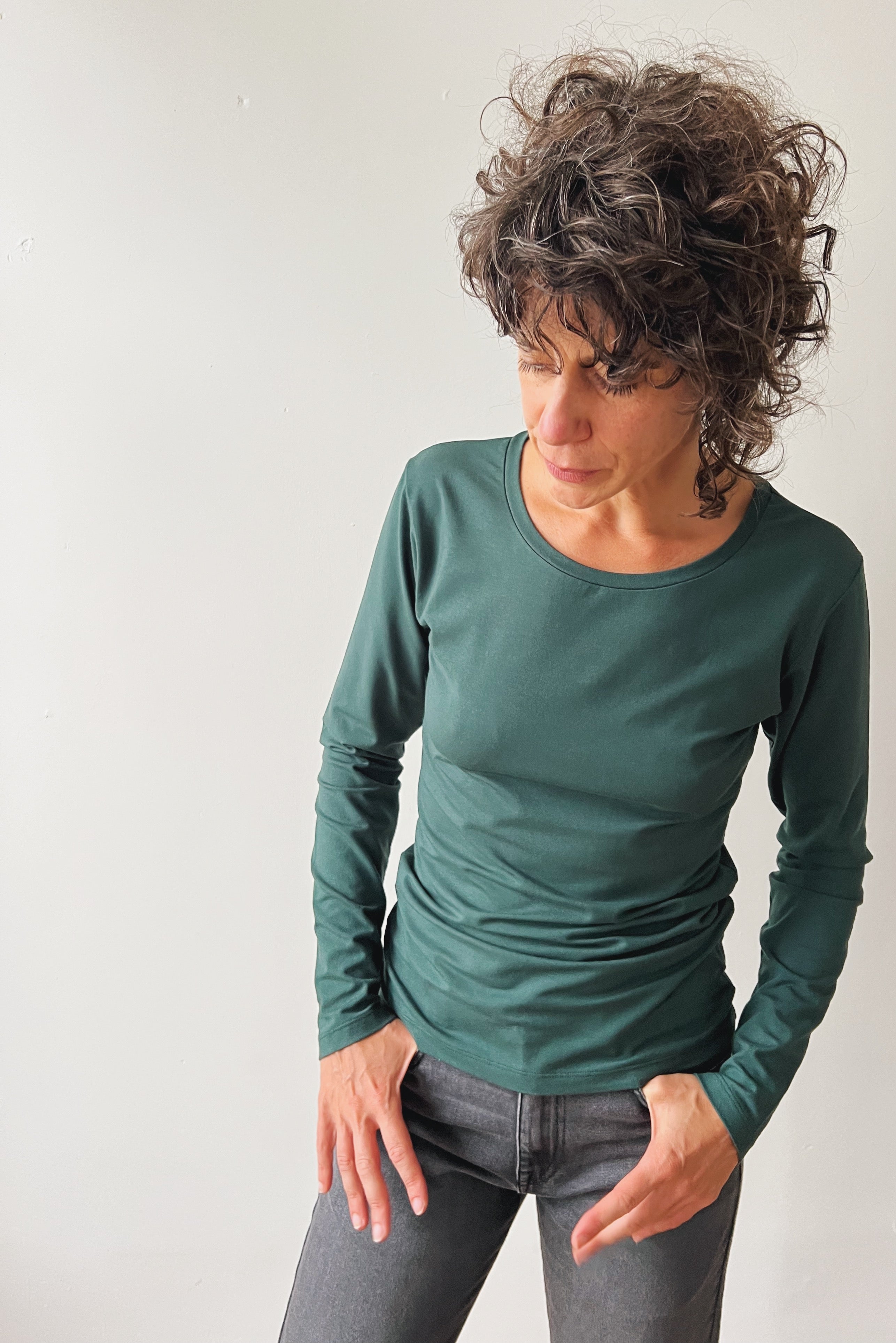 Woman wearing a pine long-sleeve and grey jeans against a plain background