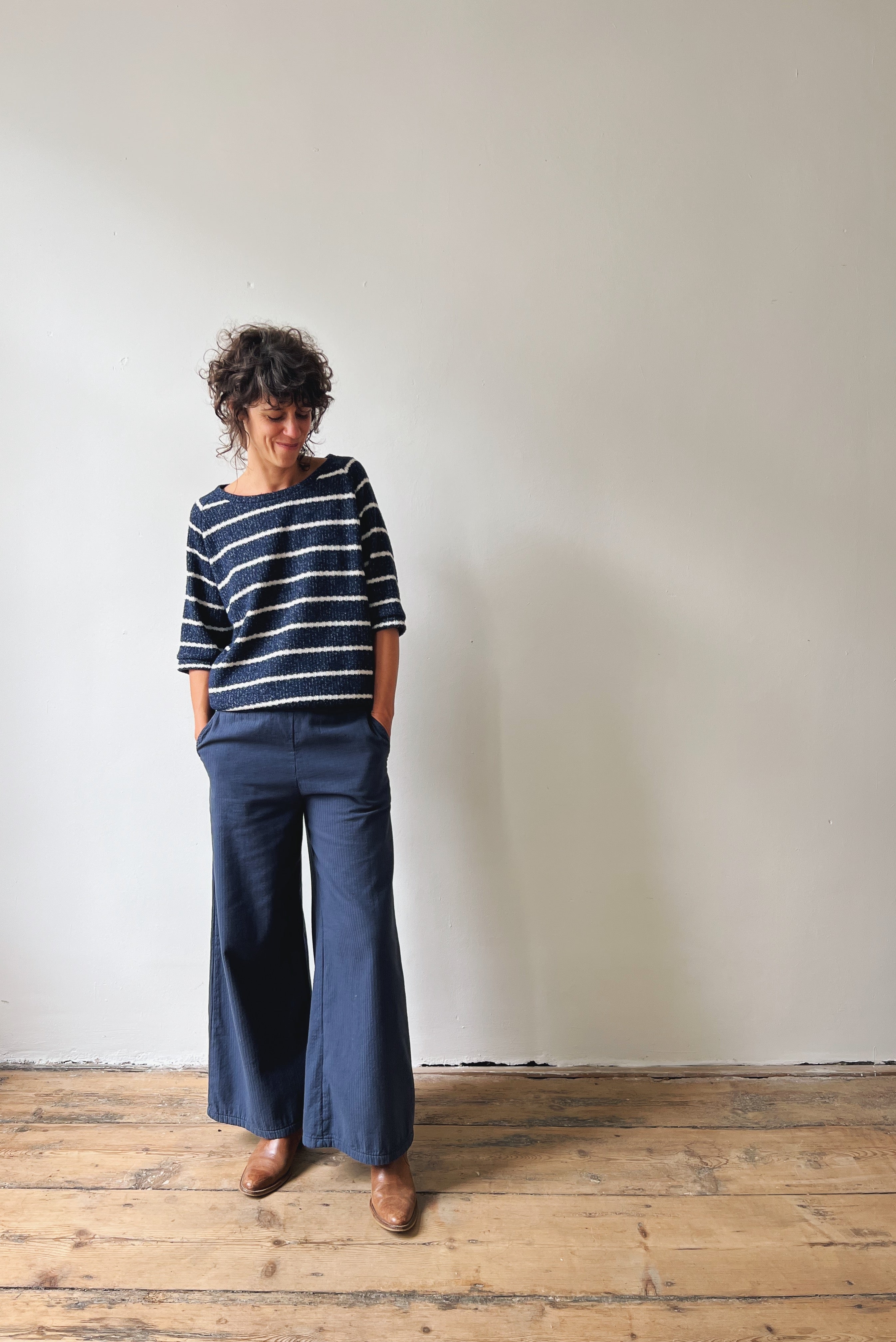Woman wearing a striped sweater and wide-leg blue pants standing against a white wall.