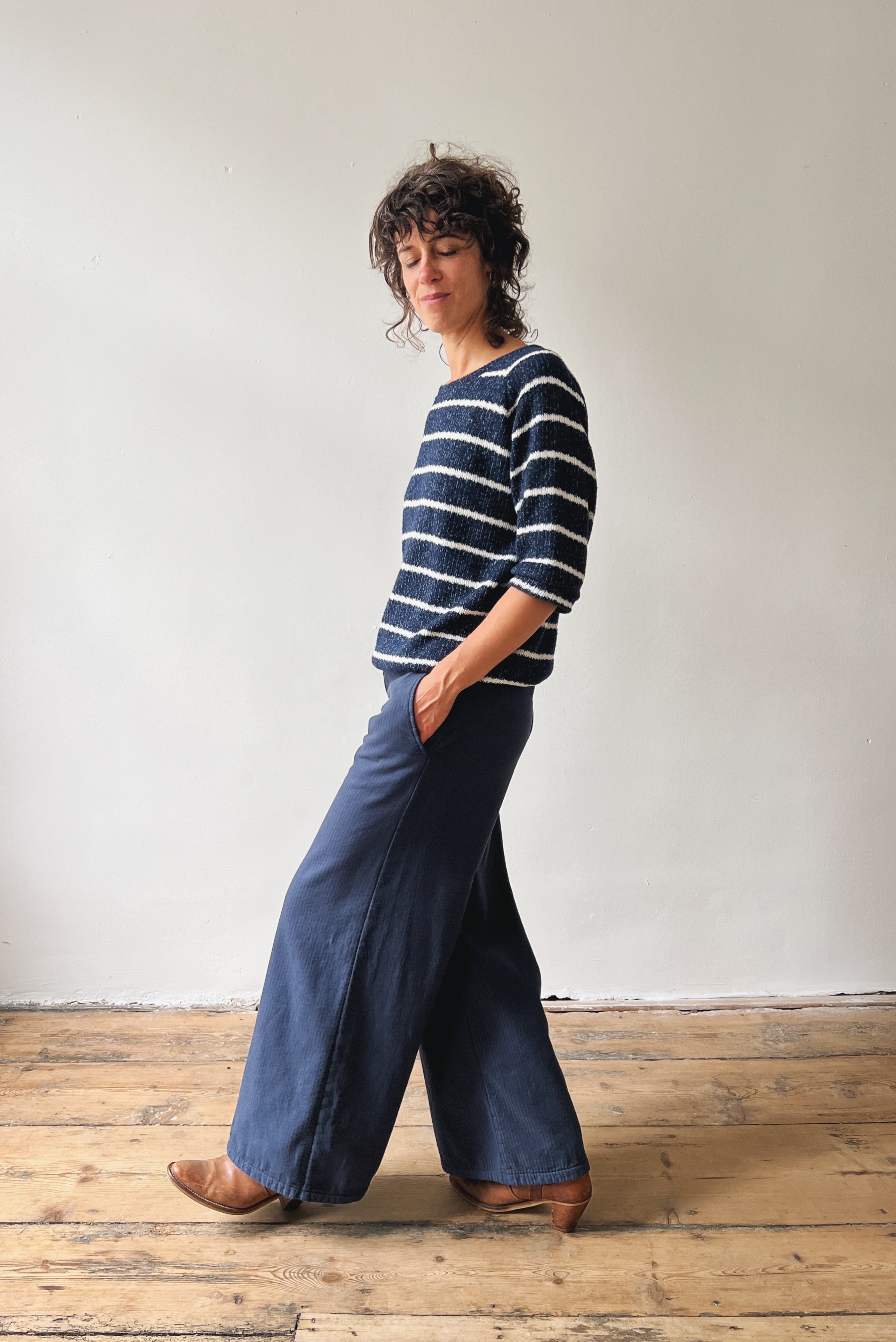 Woman wearing a striped sweater and wide-leg blue pants standing against a plain white wall.