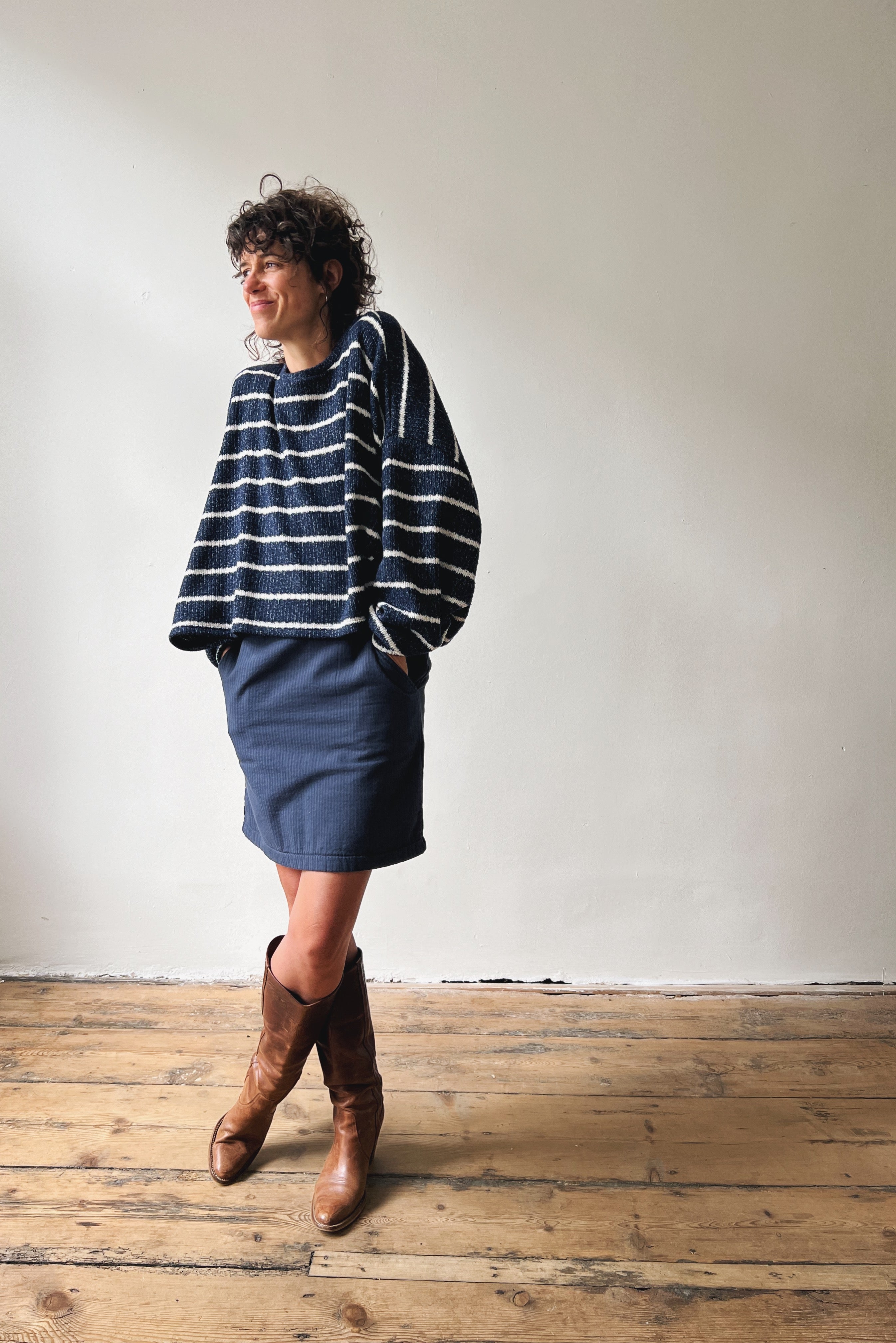 Person wearing a blue and white striped sweater and blue skirt with brown knee-high boots on a wooden floor.