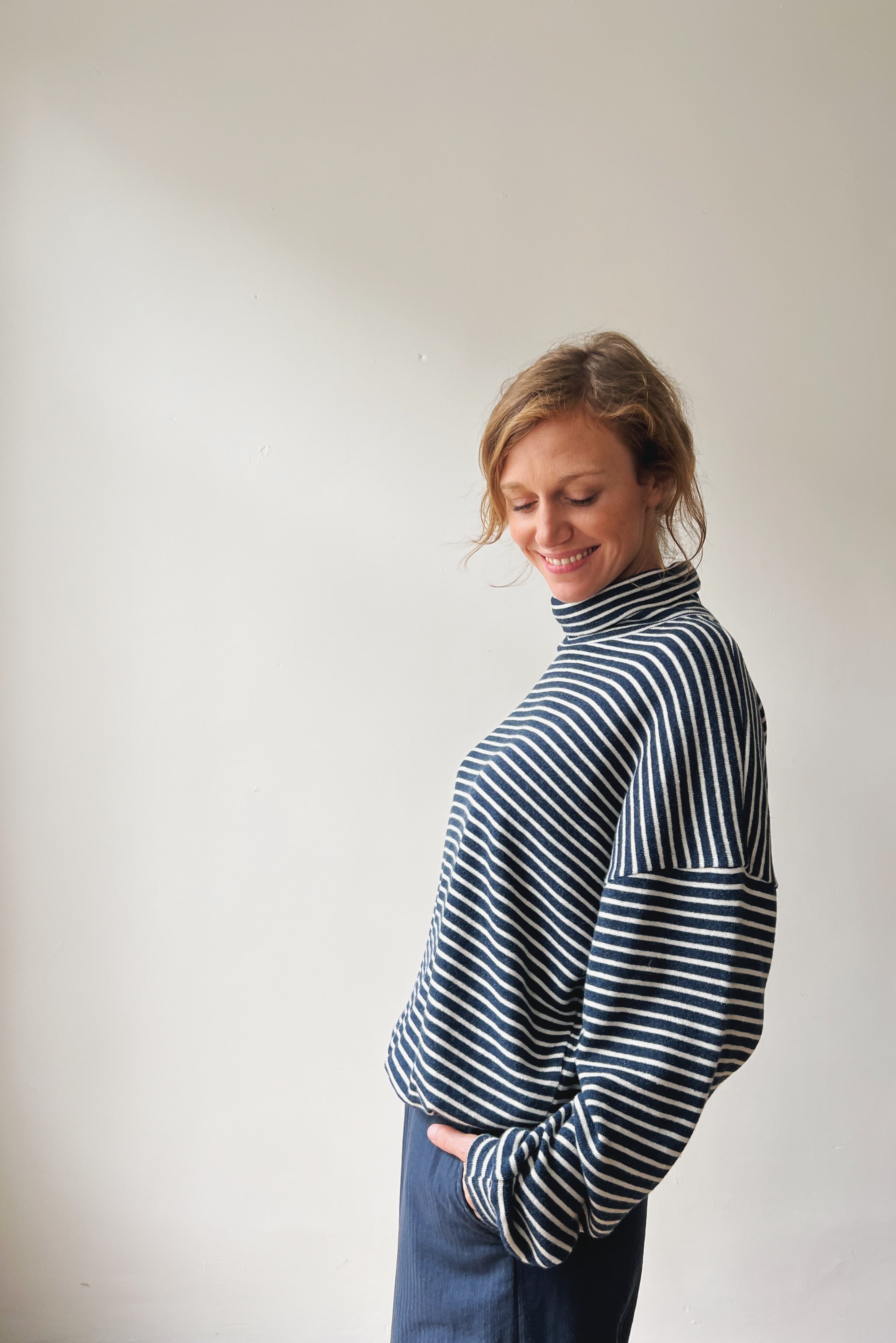 Woman wearing a black and white striped turtleneck sweater against a plain background
