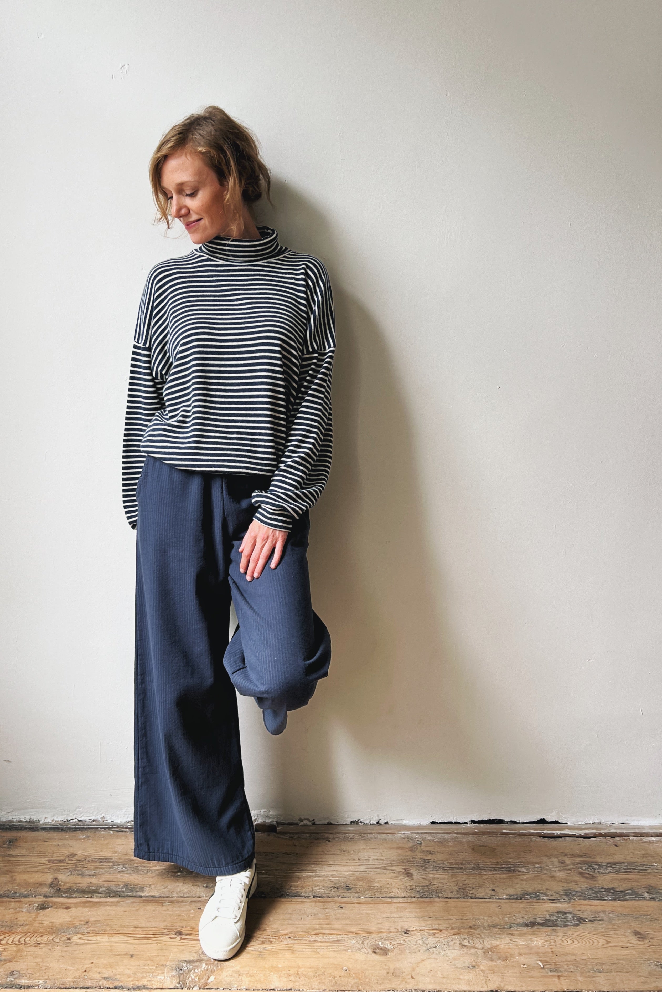 Person wearing a blue and white striped sweater and blue pants against a white wall.