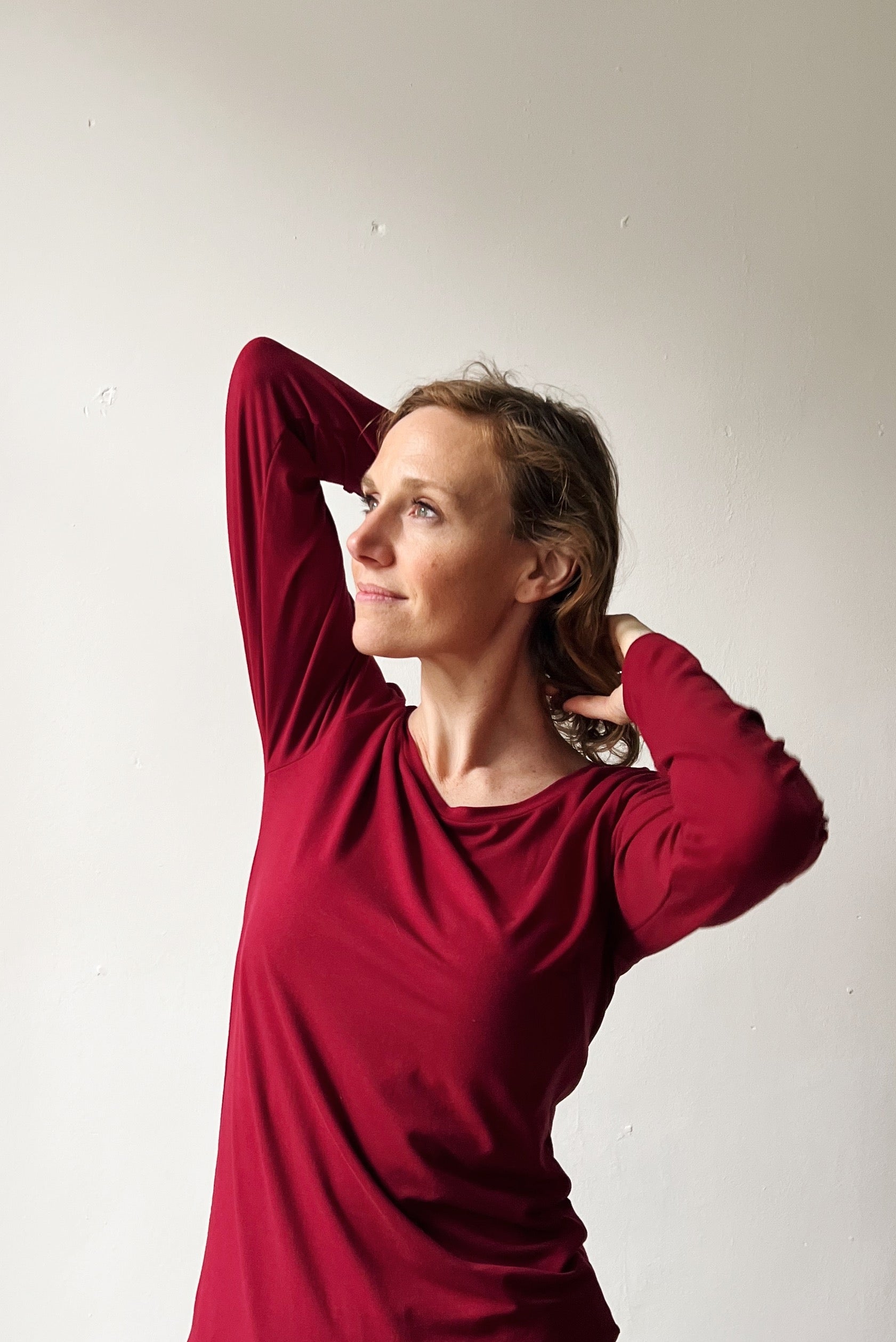 Woman wearing a red long-sleeve top against a plain background