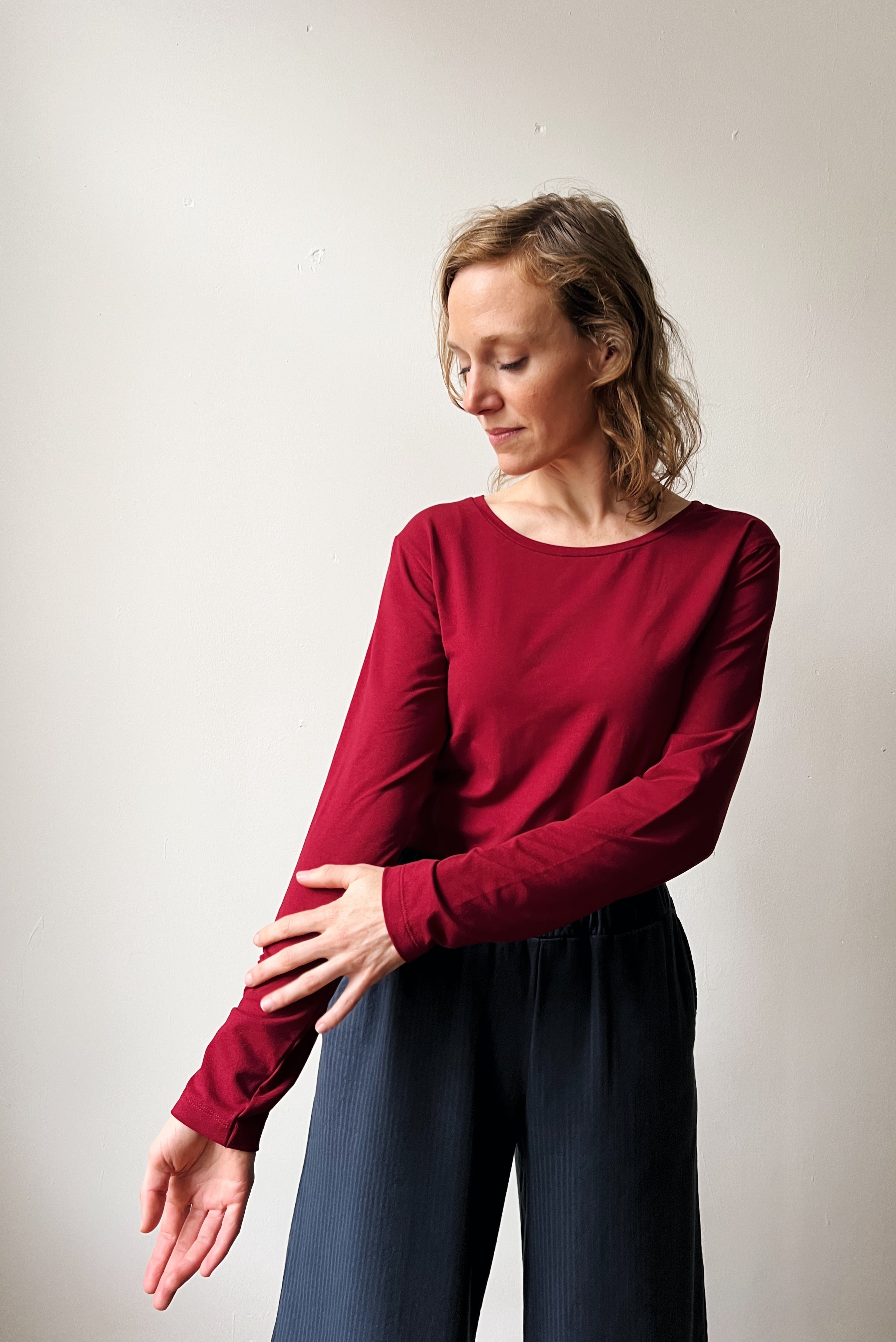 Woman wearing a red long-sleeve top and blue reversed corduroy pants against a plain background