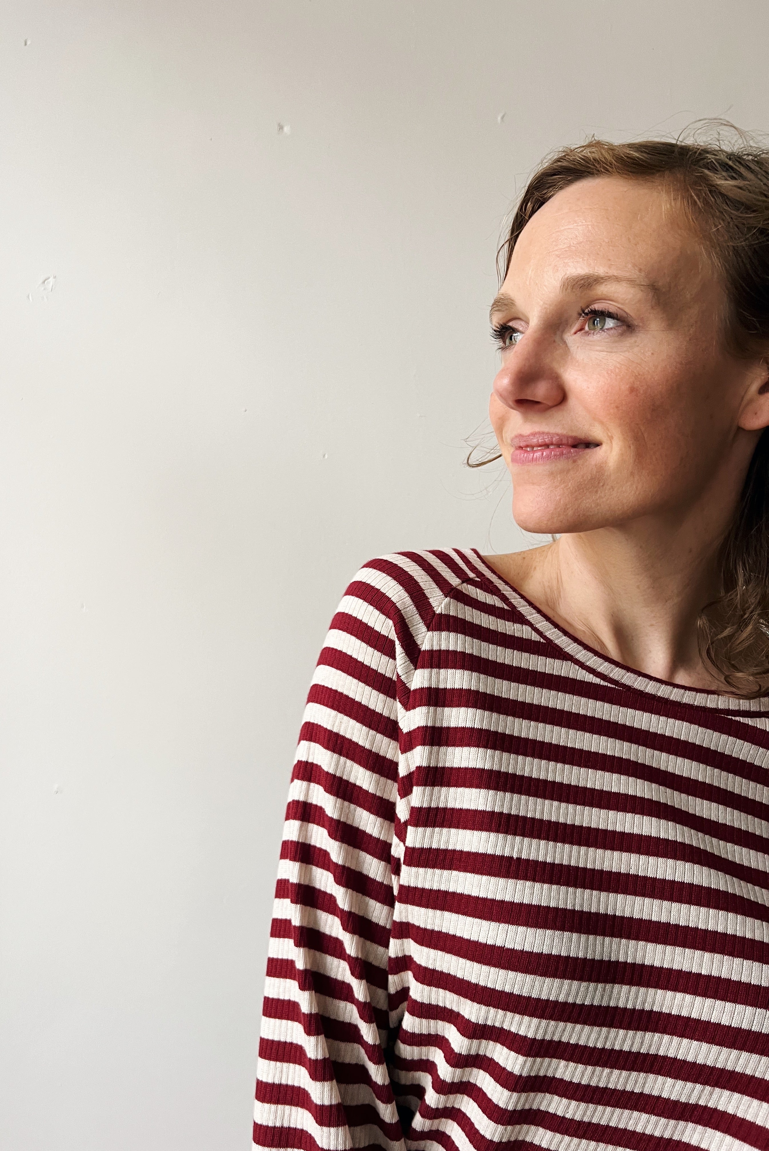 Woman wearing a red and white striped shirt against a plain background smiling softly