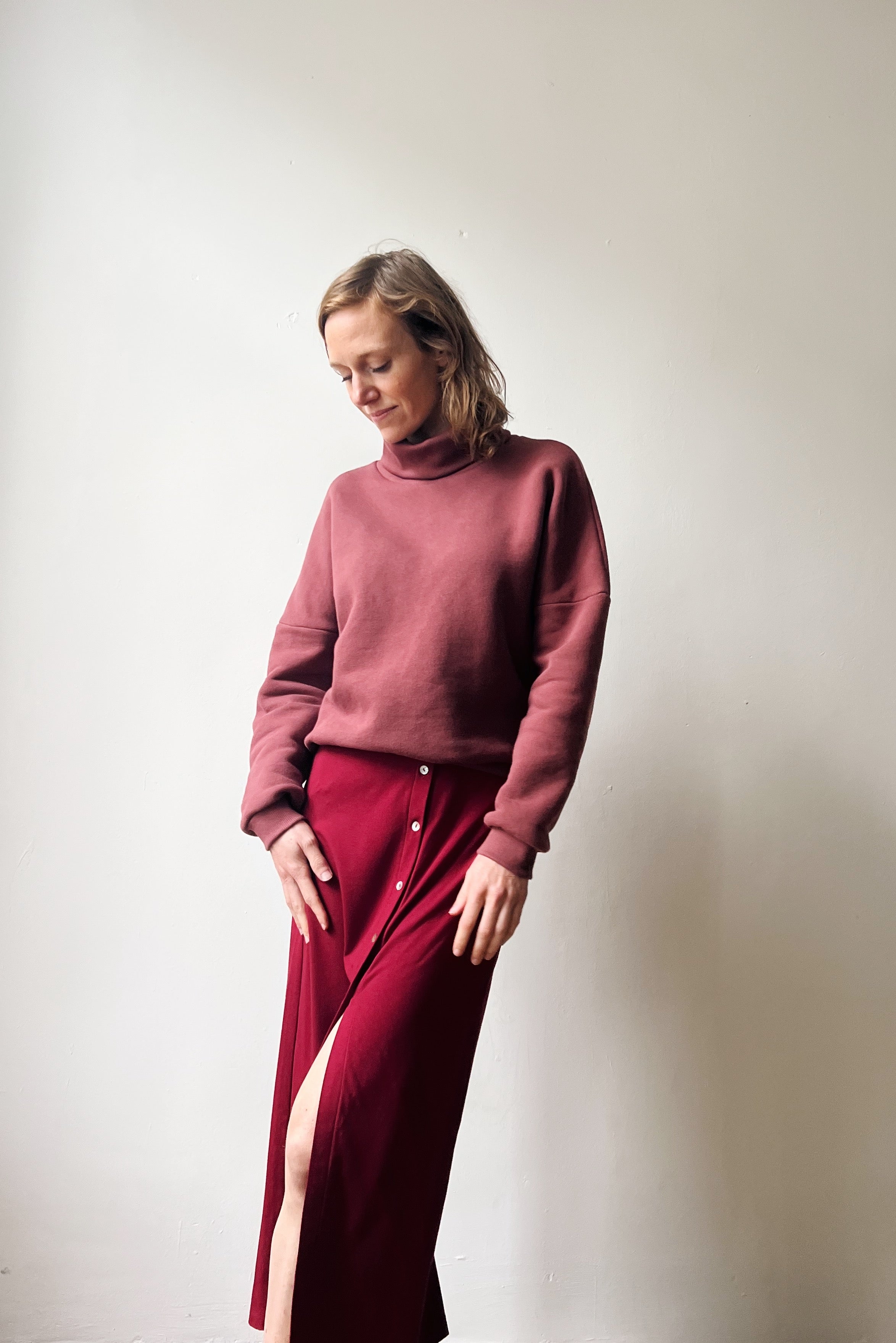 Woman wearing a figue sweater and red skirt against a plain background