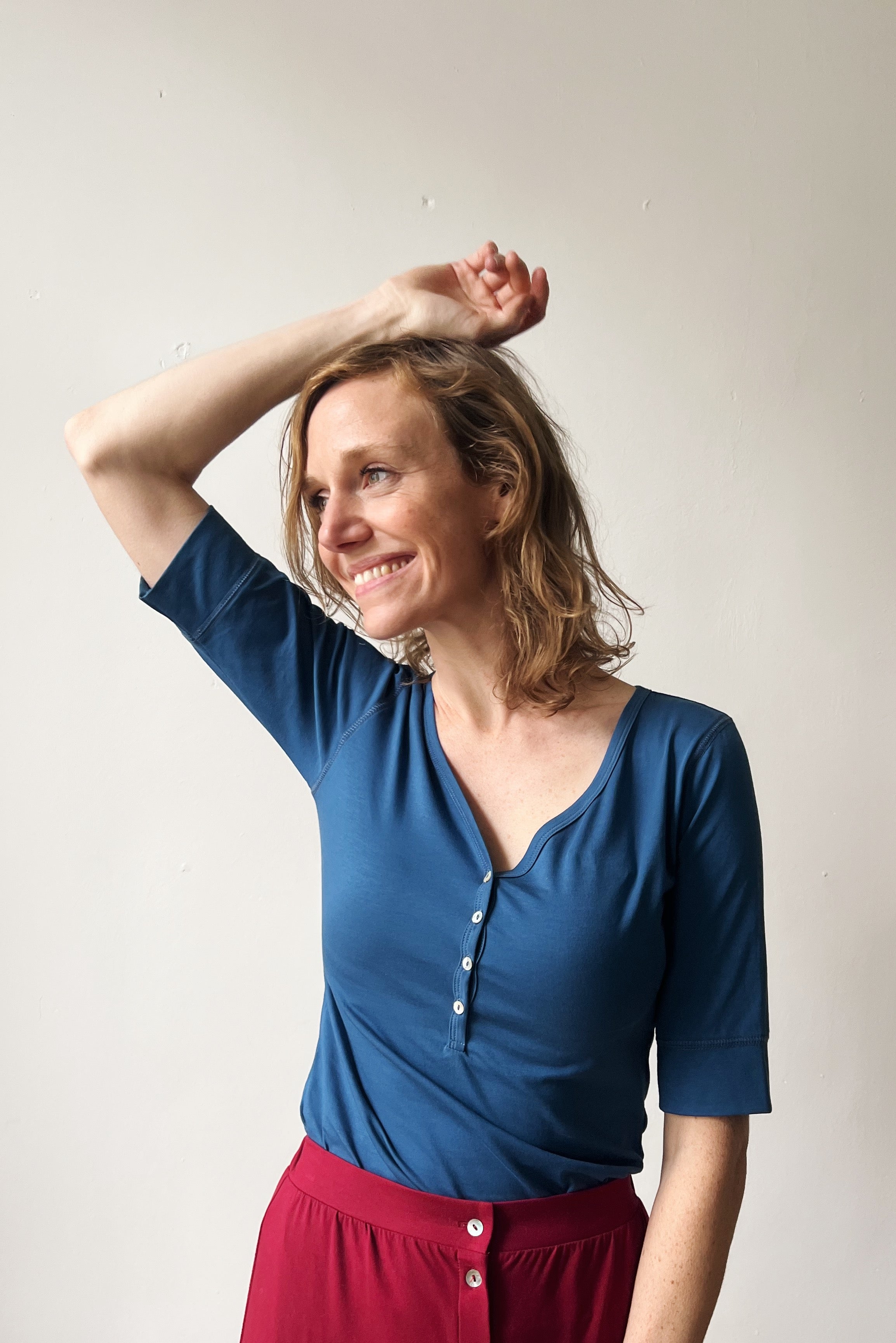 Smiling woman wearing a blue top and red skirt against a plain background