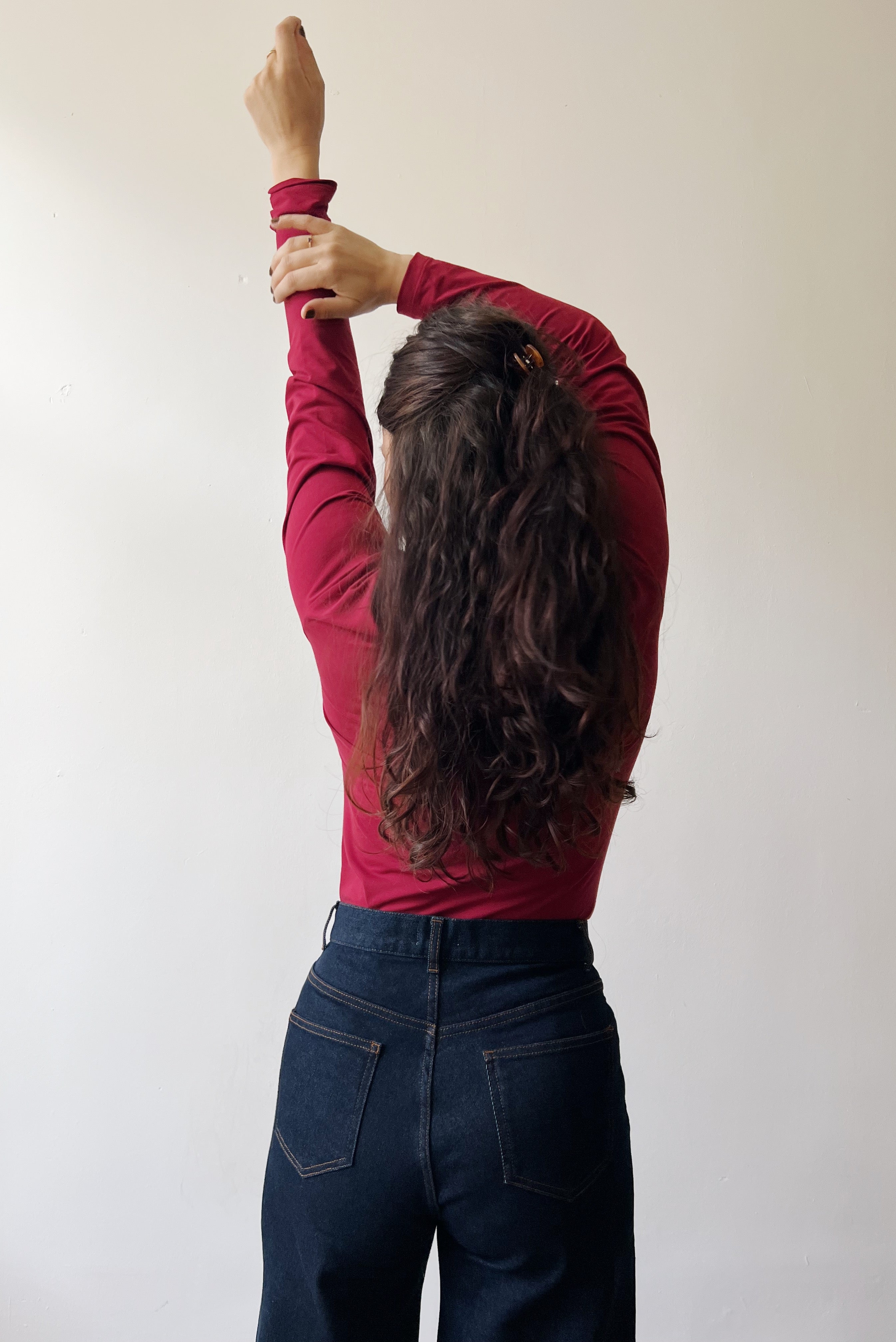 Person wearing a red long-sleeve shirt and dark jeans against a plain background