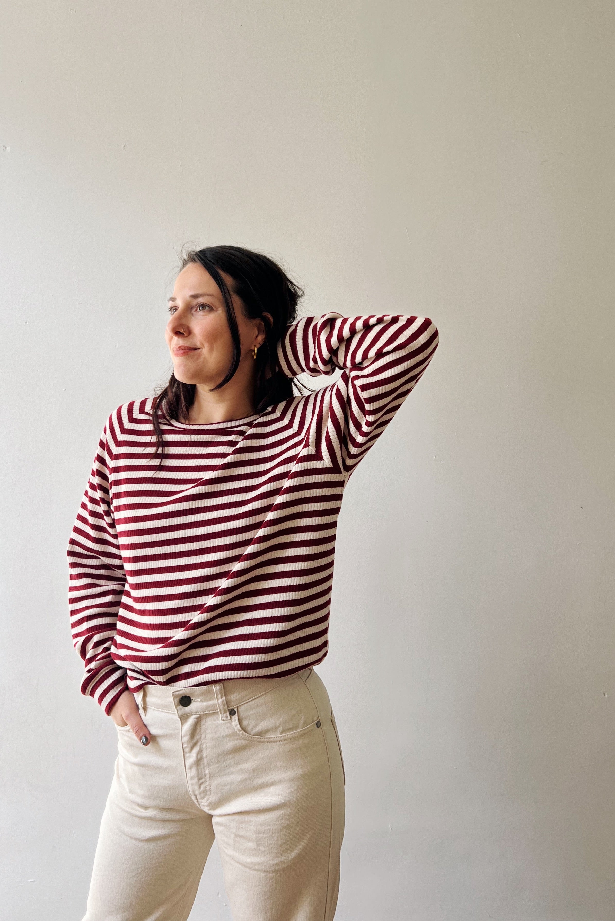 Person wearing a red and white striped sweater and white pants against a plain background