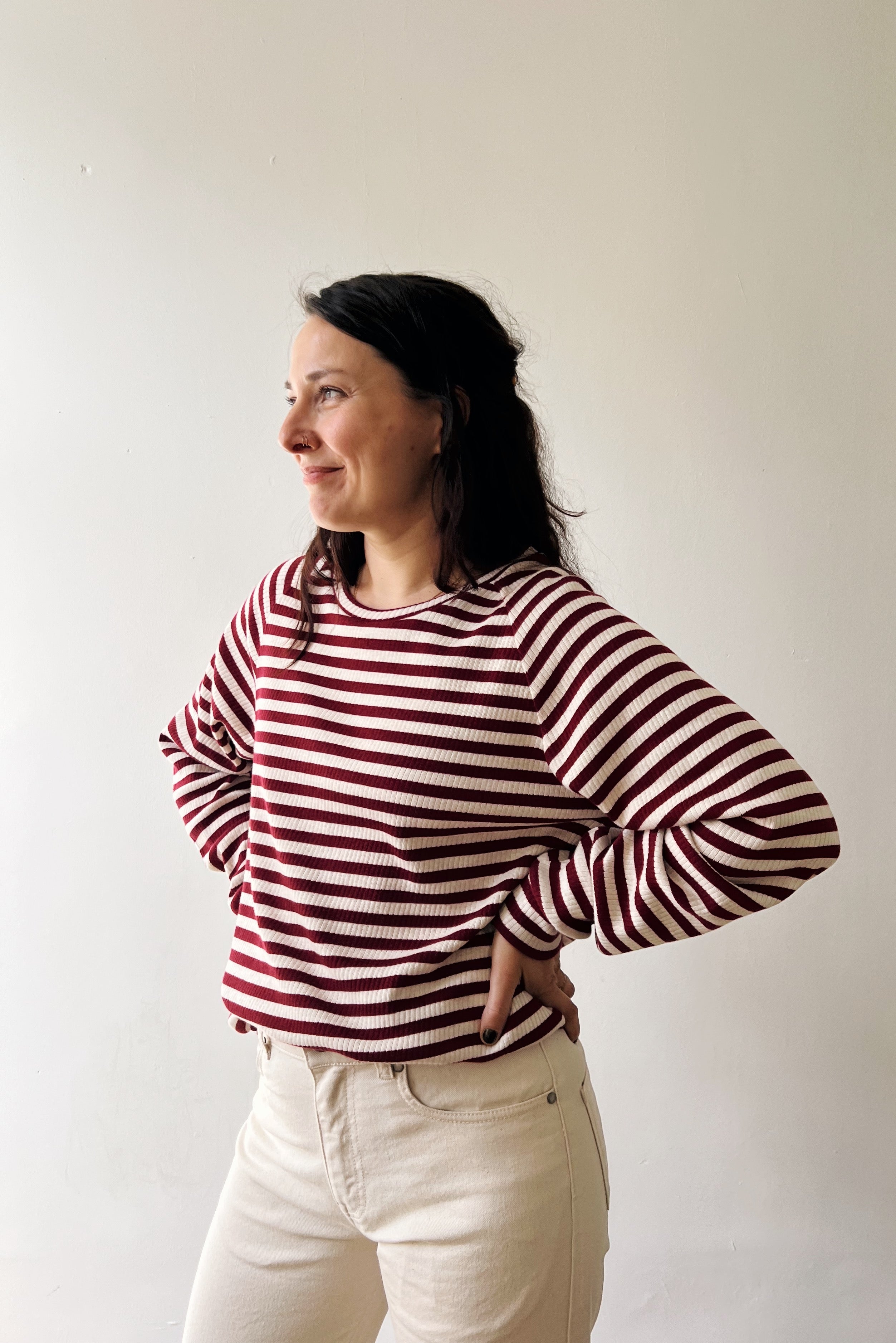 Woman wearing a red and white striped shirt and white jeans against a plain background