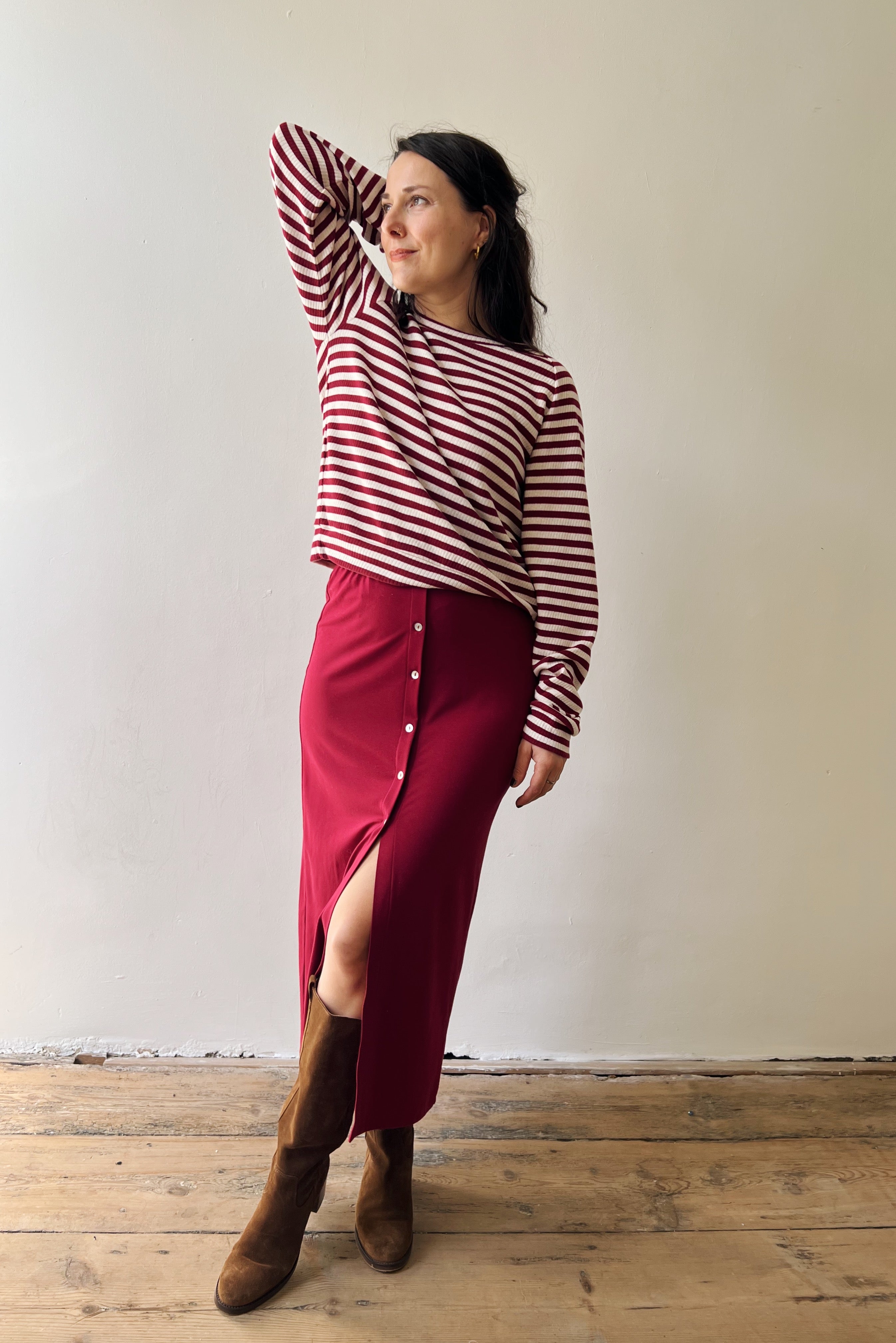 Woman wearing a red and white striped sweater and red skirt with brown kneeboots against a plain background