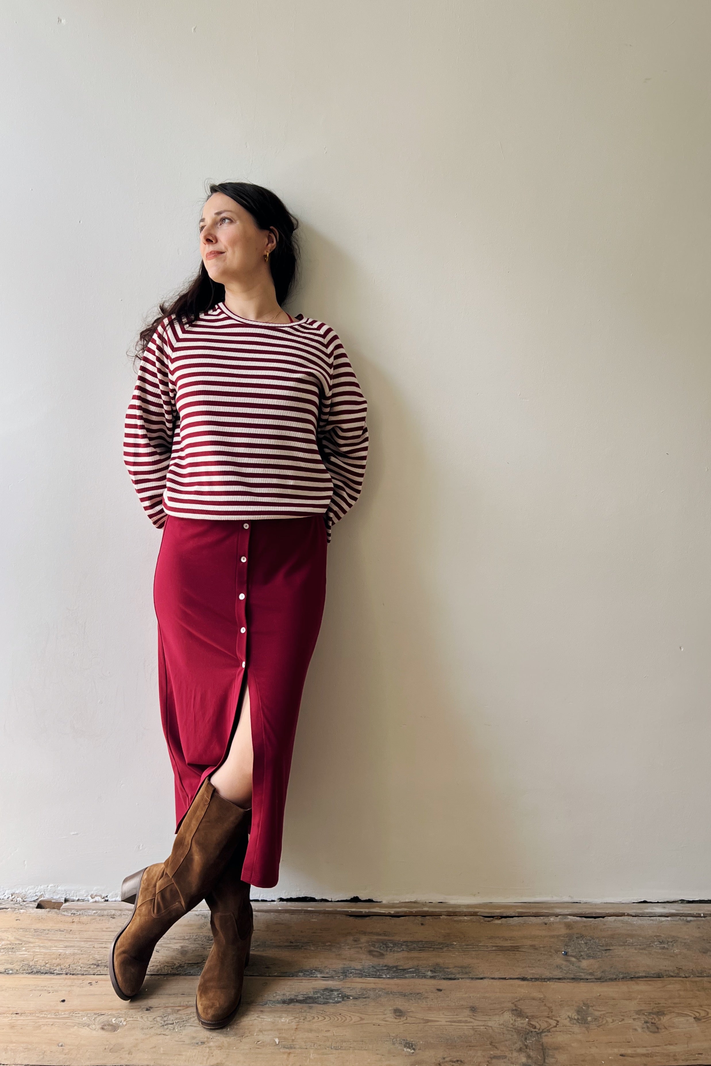 Woman wearing a red and white striped sweater and red skirt against a plain wall.