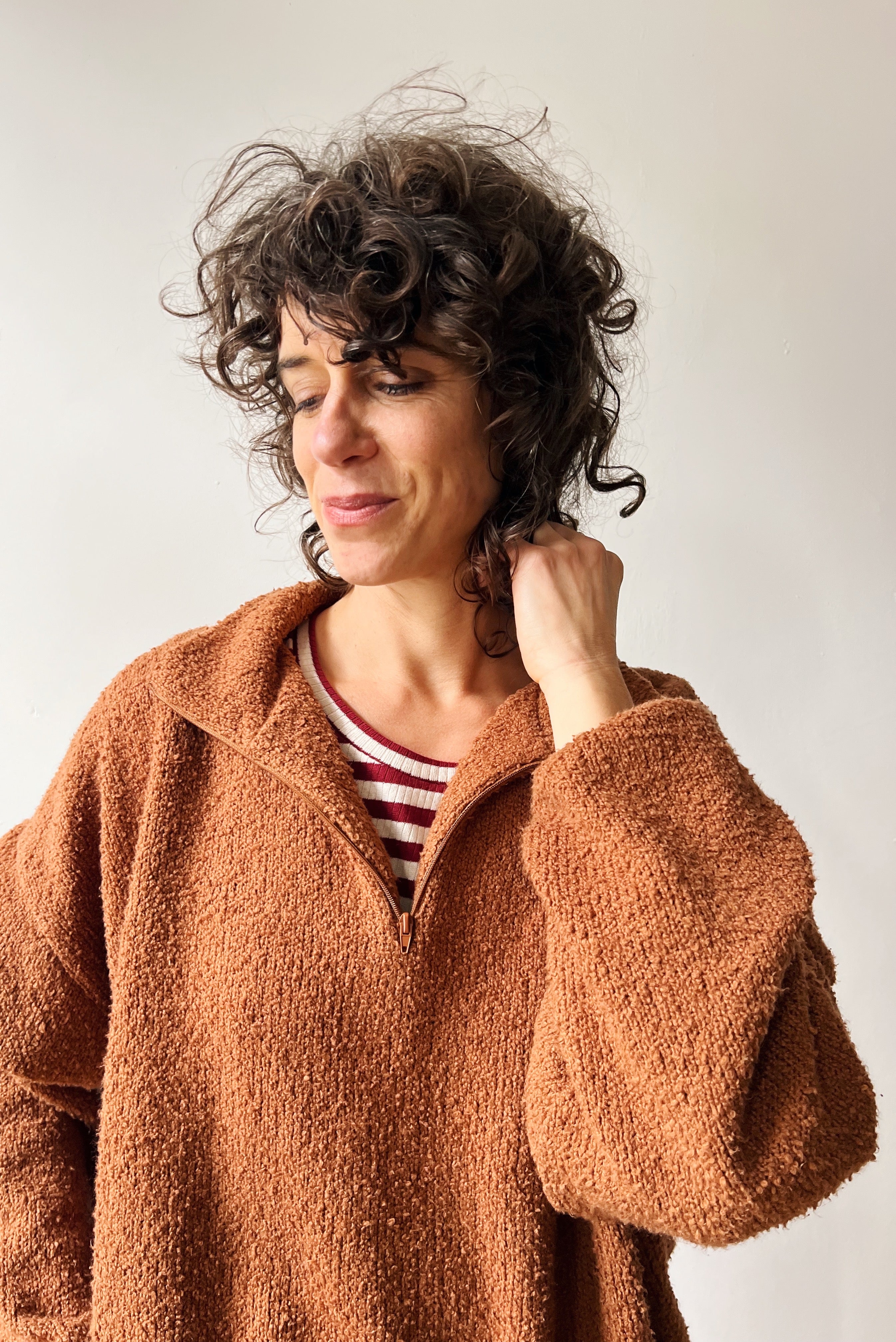 Woman wearing a brown teddy sweater with zip-up closure over a red&white striped shirt with a plain background