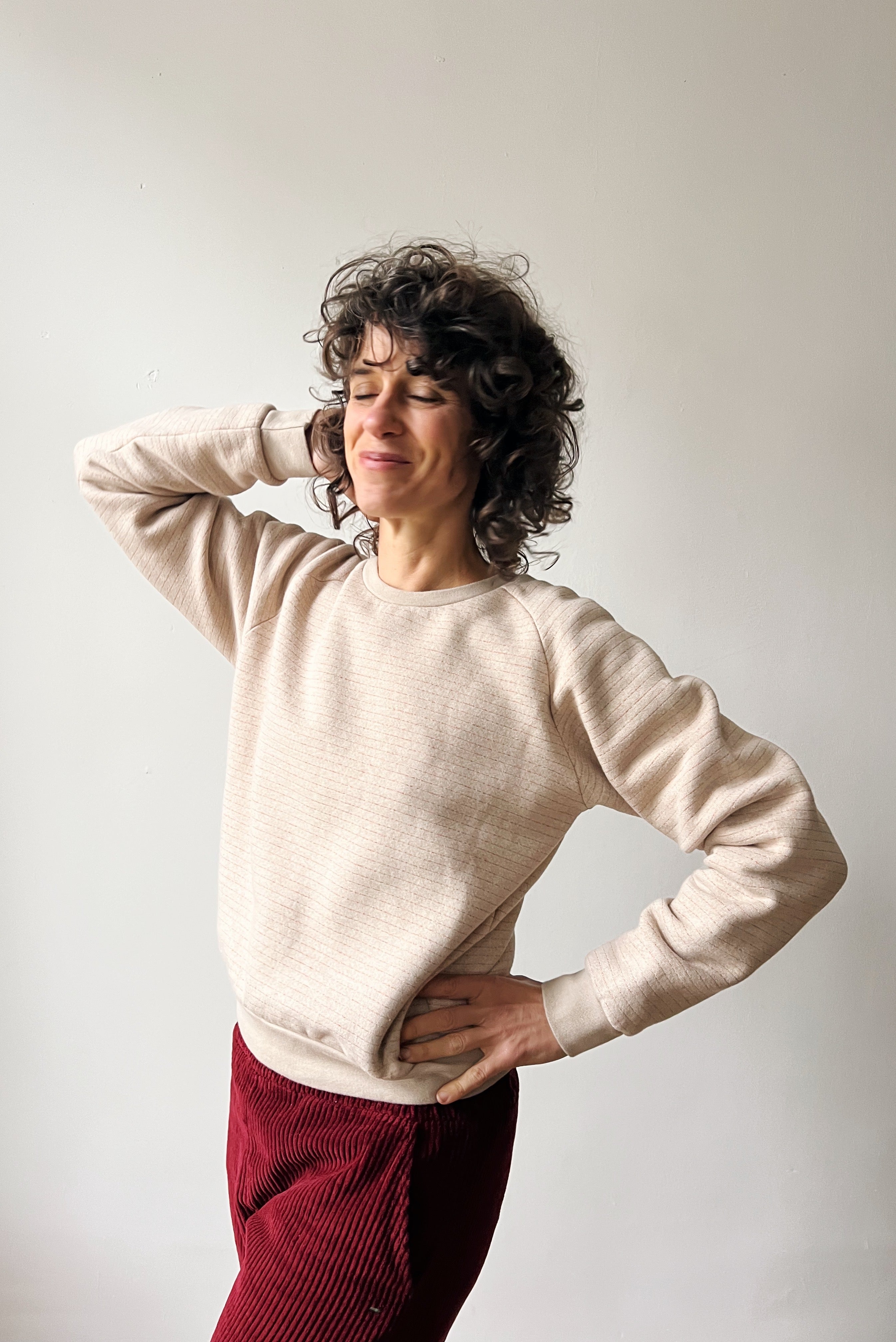 Woman wearing a beige sweater and red pants against a plain background