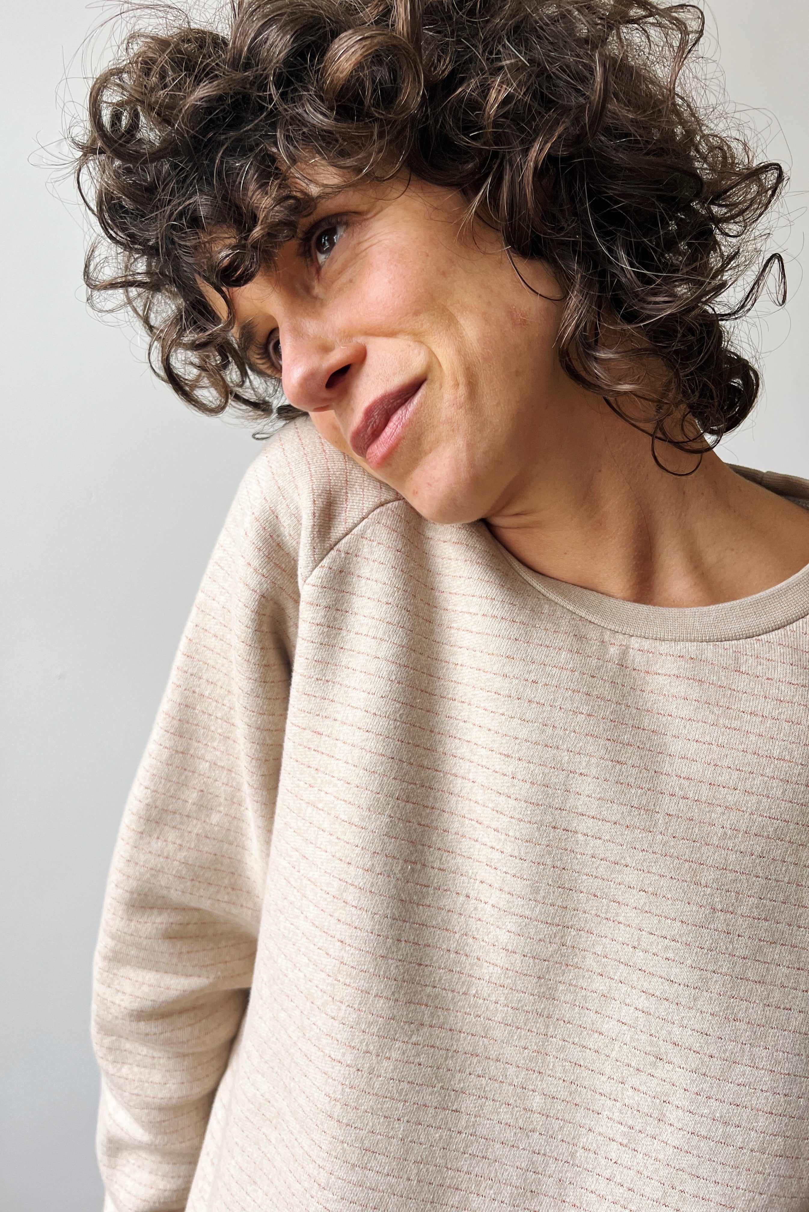 Woman wearing a beige sweater with a subtle bronze stripe against a plain background