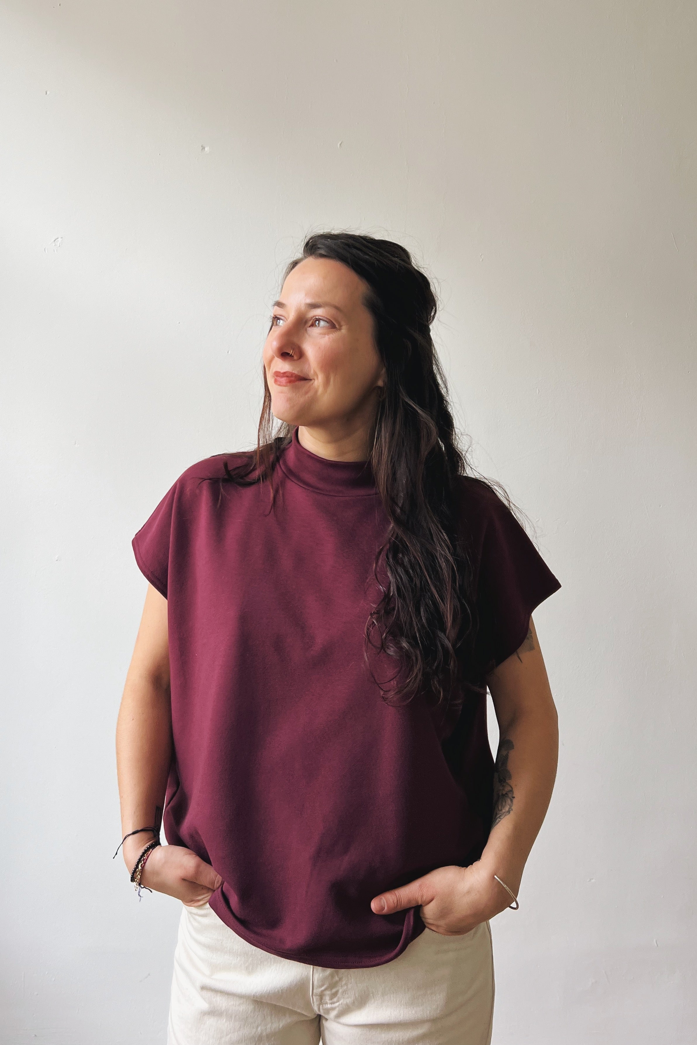 Woman wearing an aubergine sleeveless sweater against a plain background