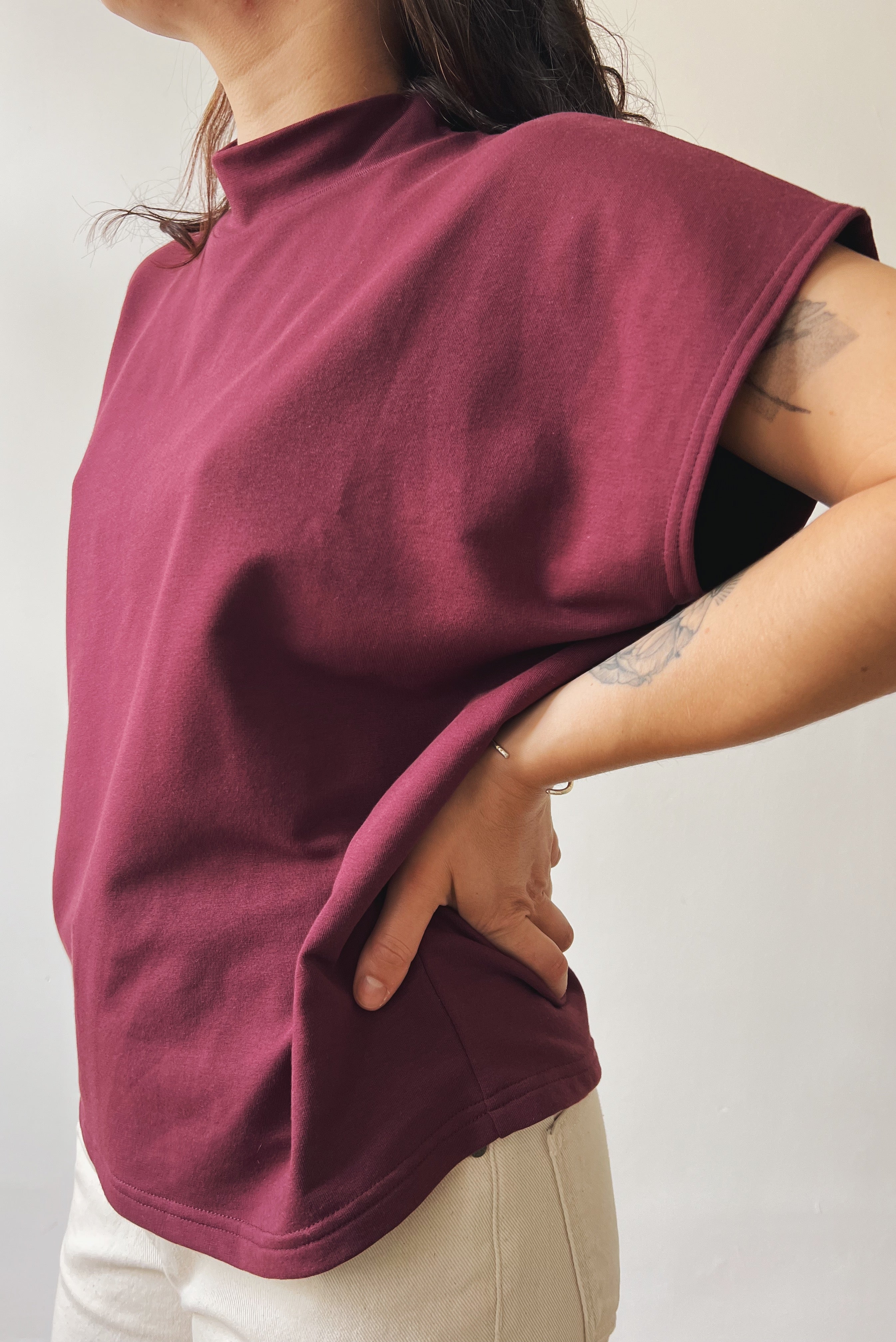 Person wearing an aubergine sleeveless sweater against a plain background