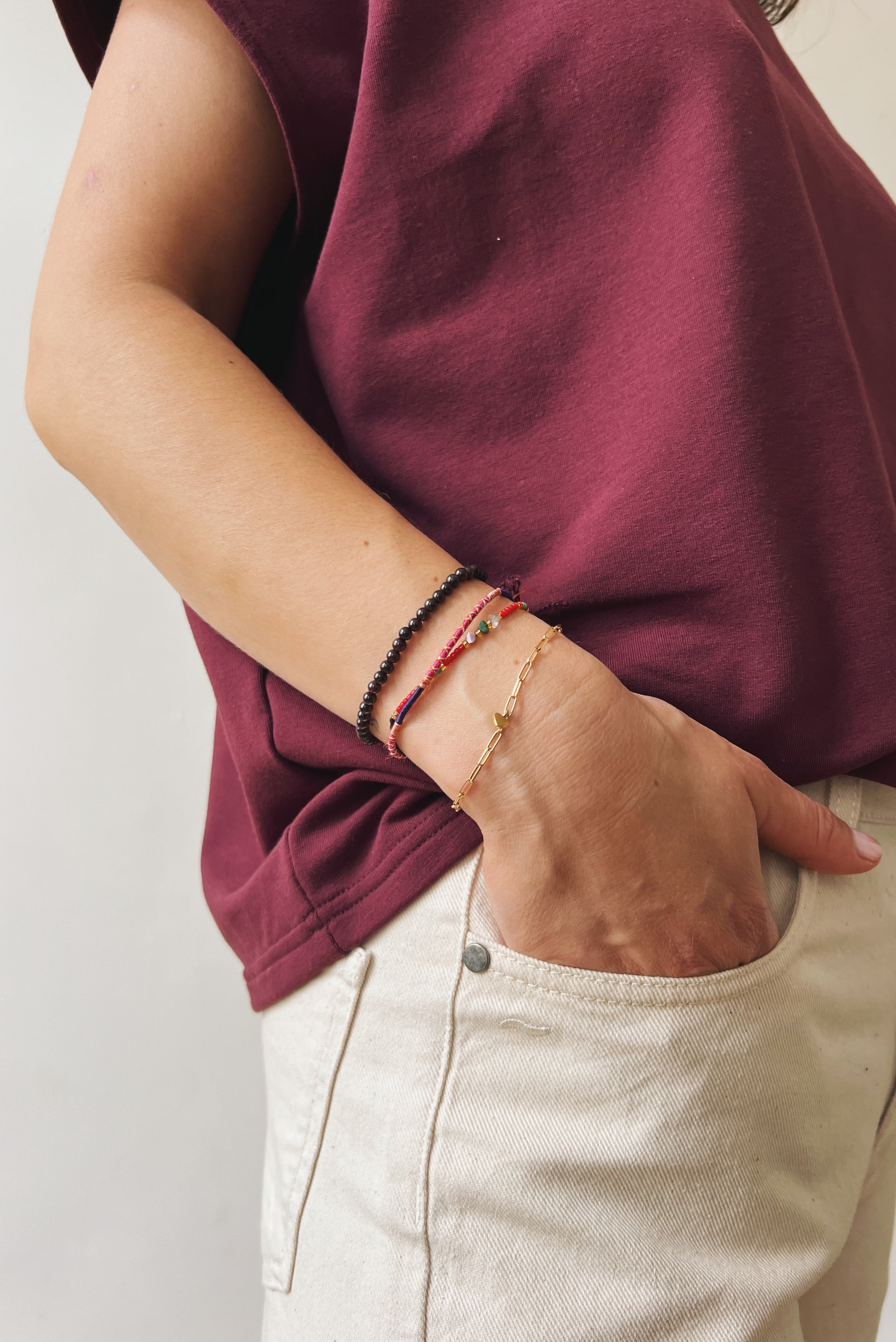 Person wearing an aubergine shirt and oat jeans with visible bracelets on a plain background
