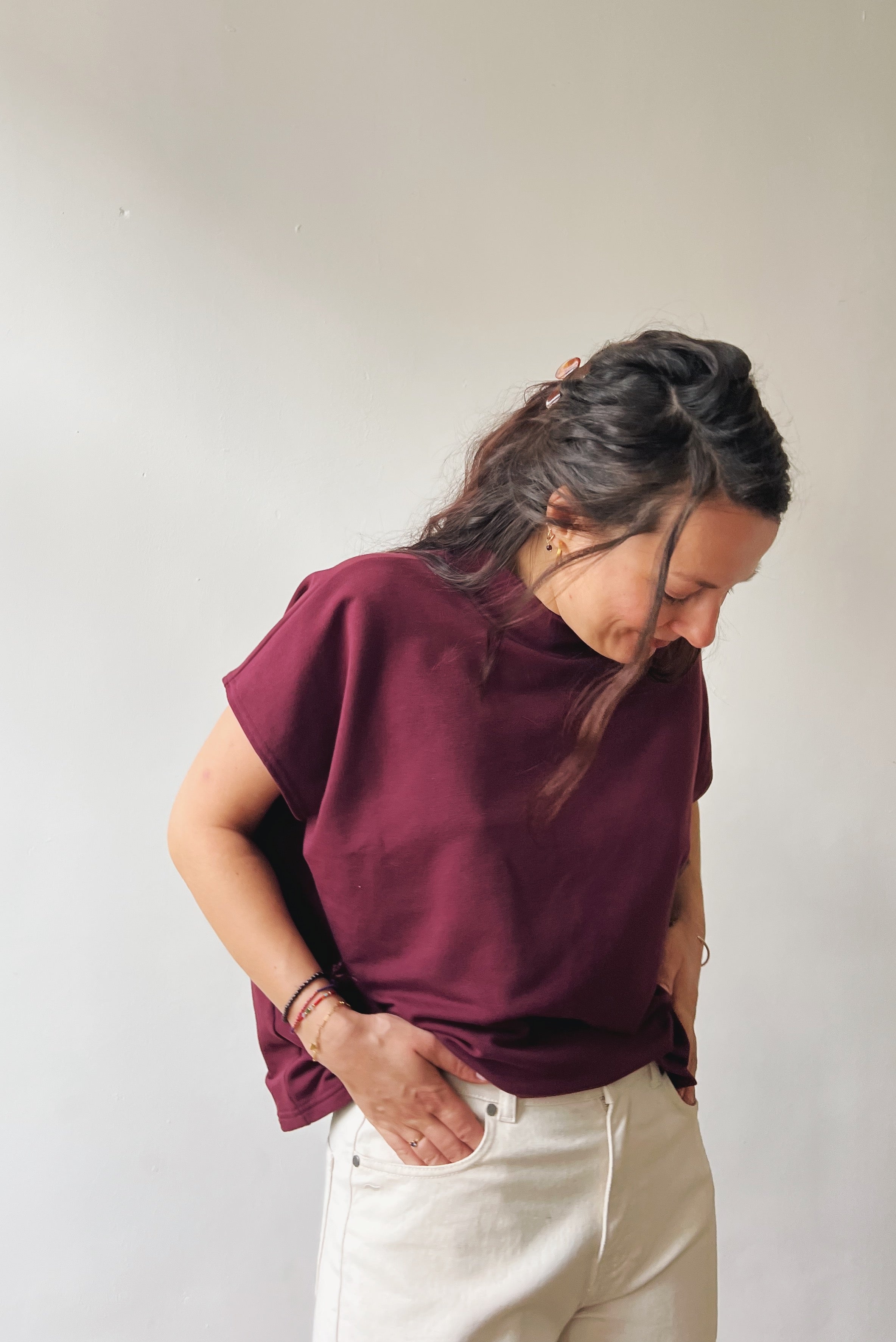 Person wearing an aubergine sleeveless sweater and oat jeans