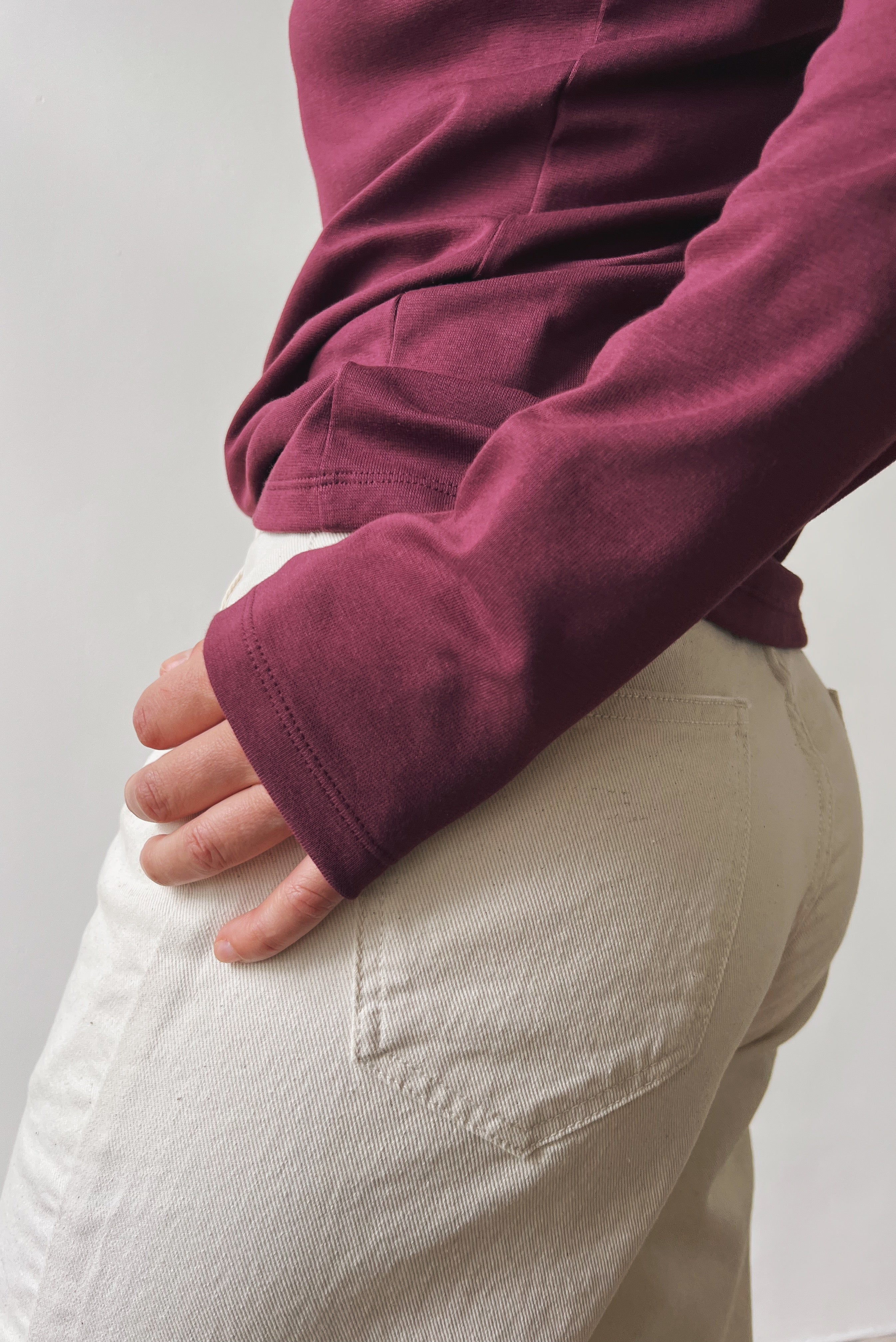 Person wearing an aubergine longsleeve shirt and oat jeans against a white background