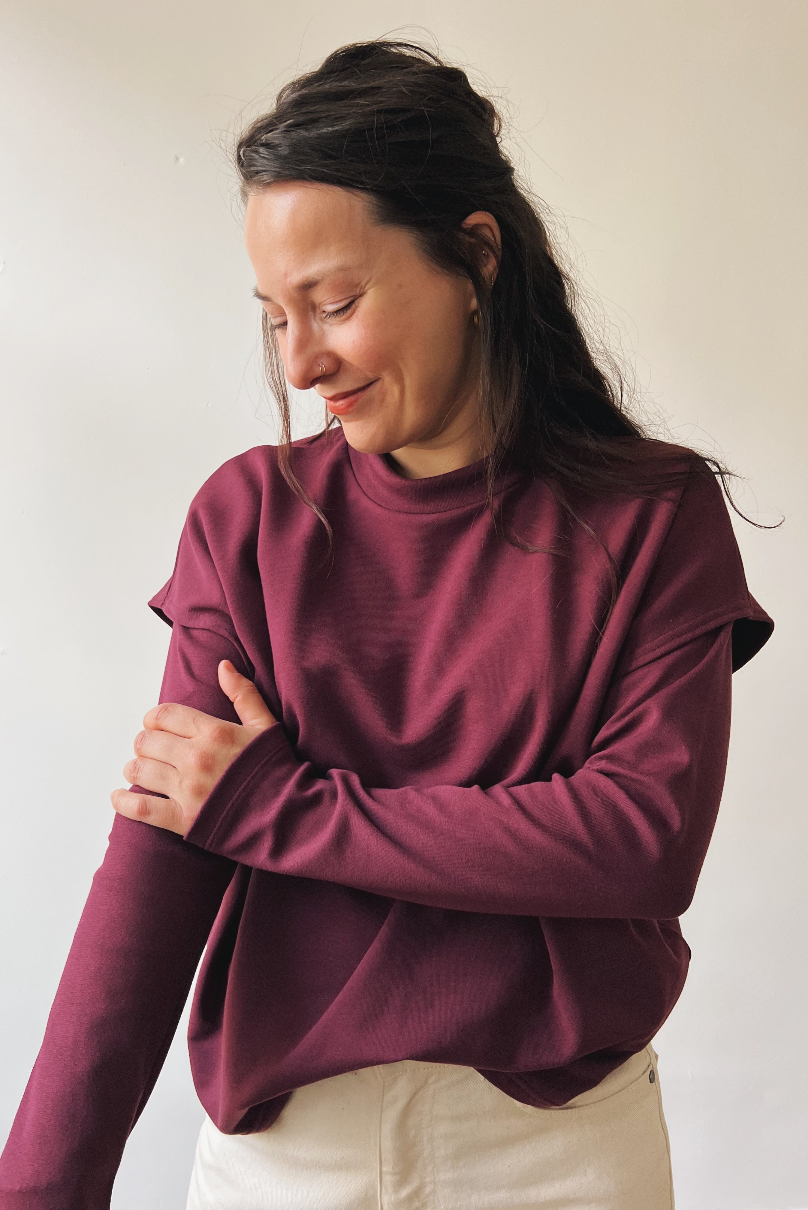 Woman wearing an aubergine longsleeve en sleeveless sweater against a plain background