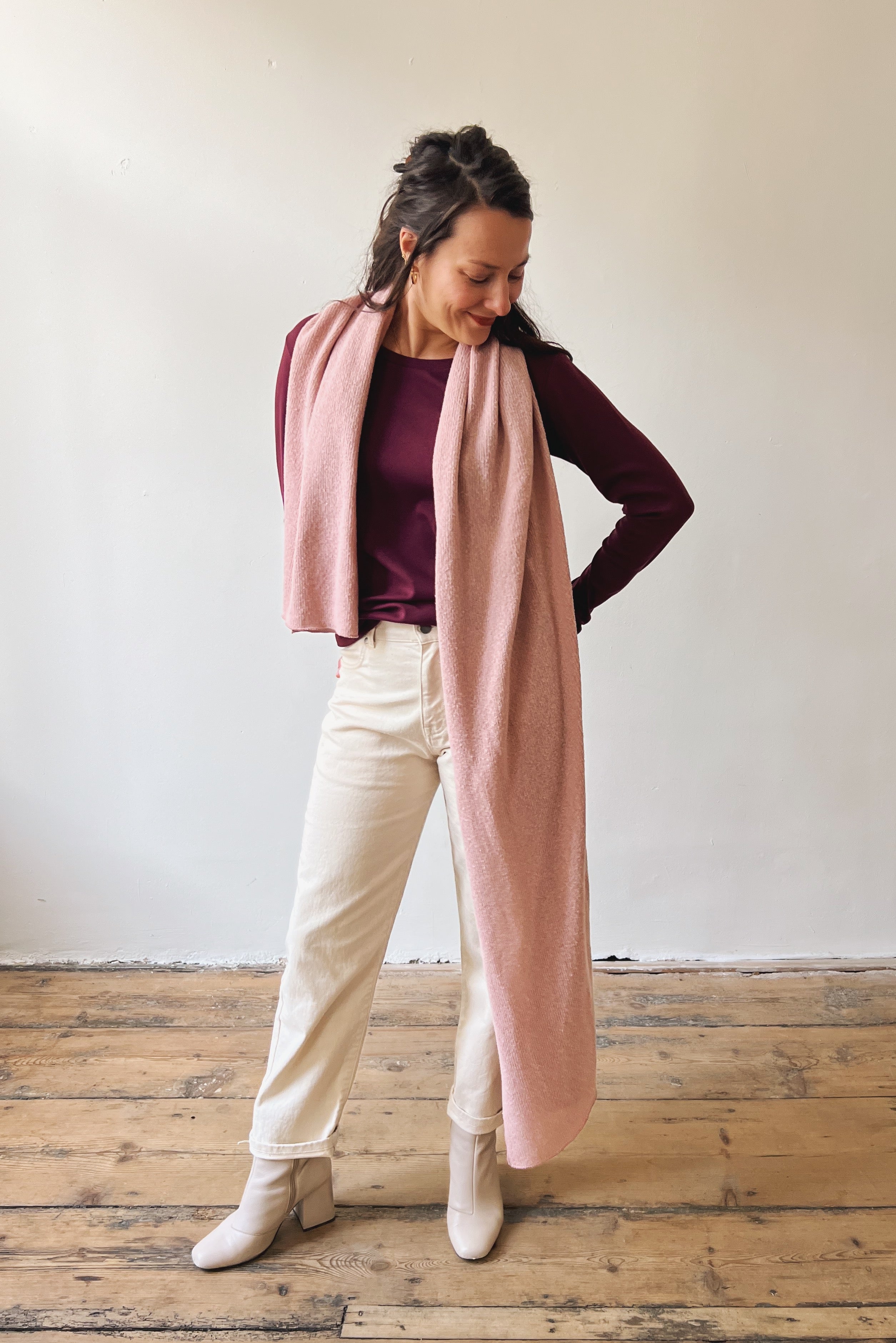 Woman wearing a long pink scarf, aubergine longsleeve, and an oat boyfriend jeans.