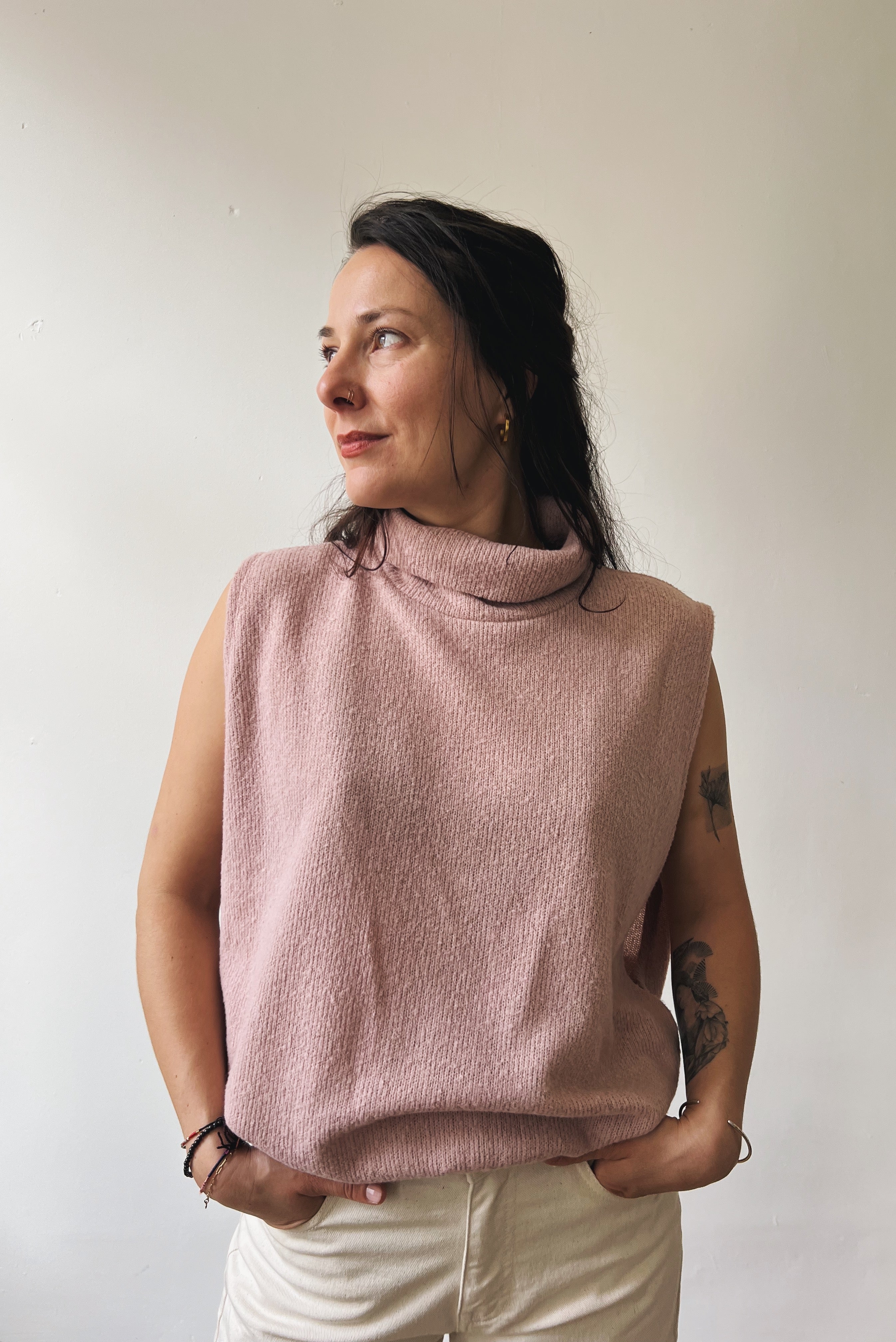 Woman wearing a pink sleeveless sweater against a plain background