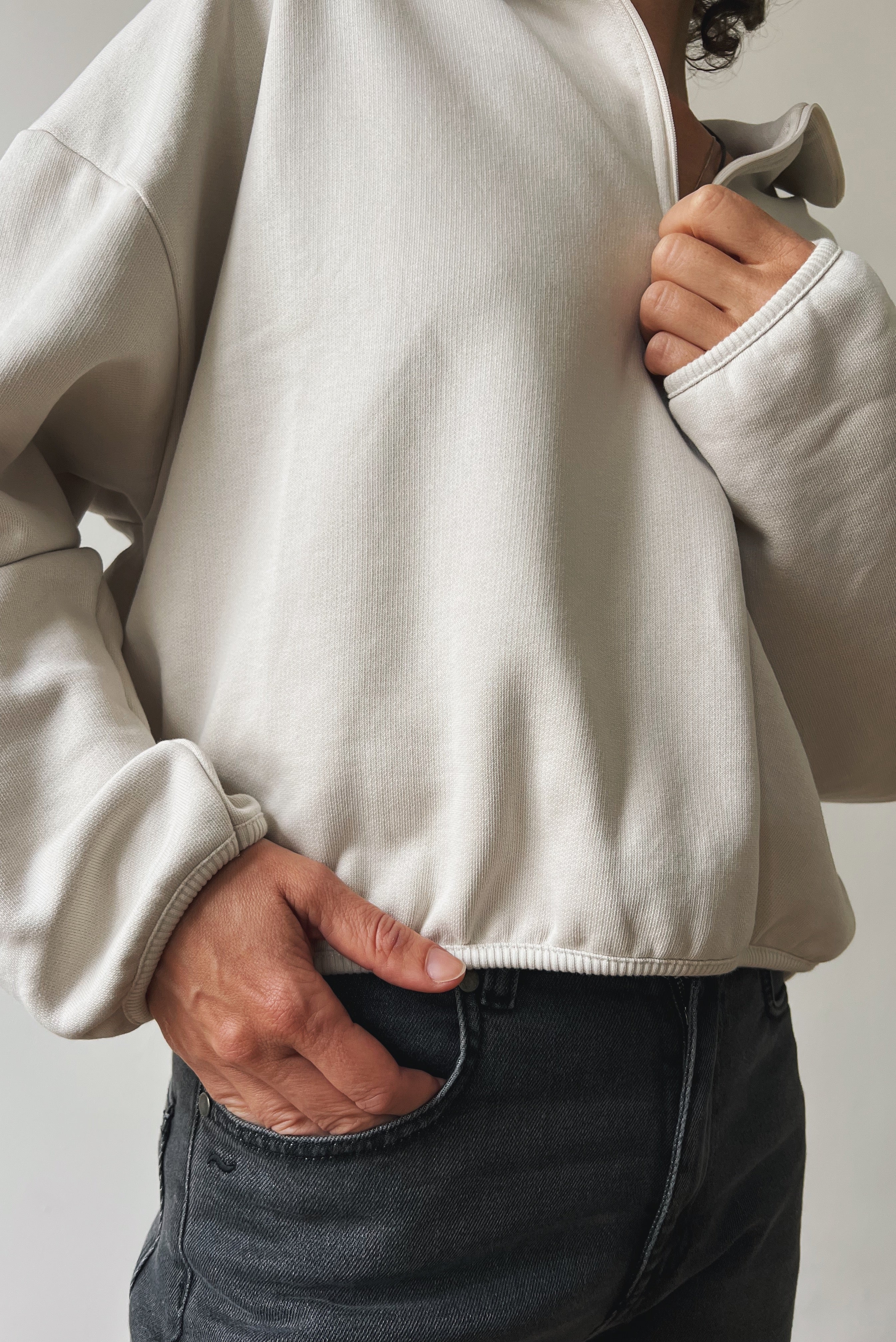 Person wearing a beige sweater and grey jeans against a neutral background