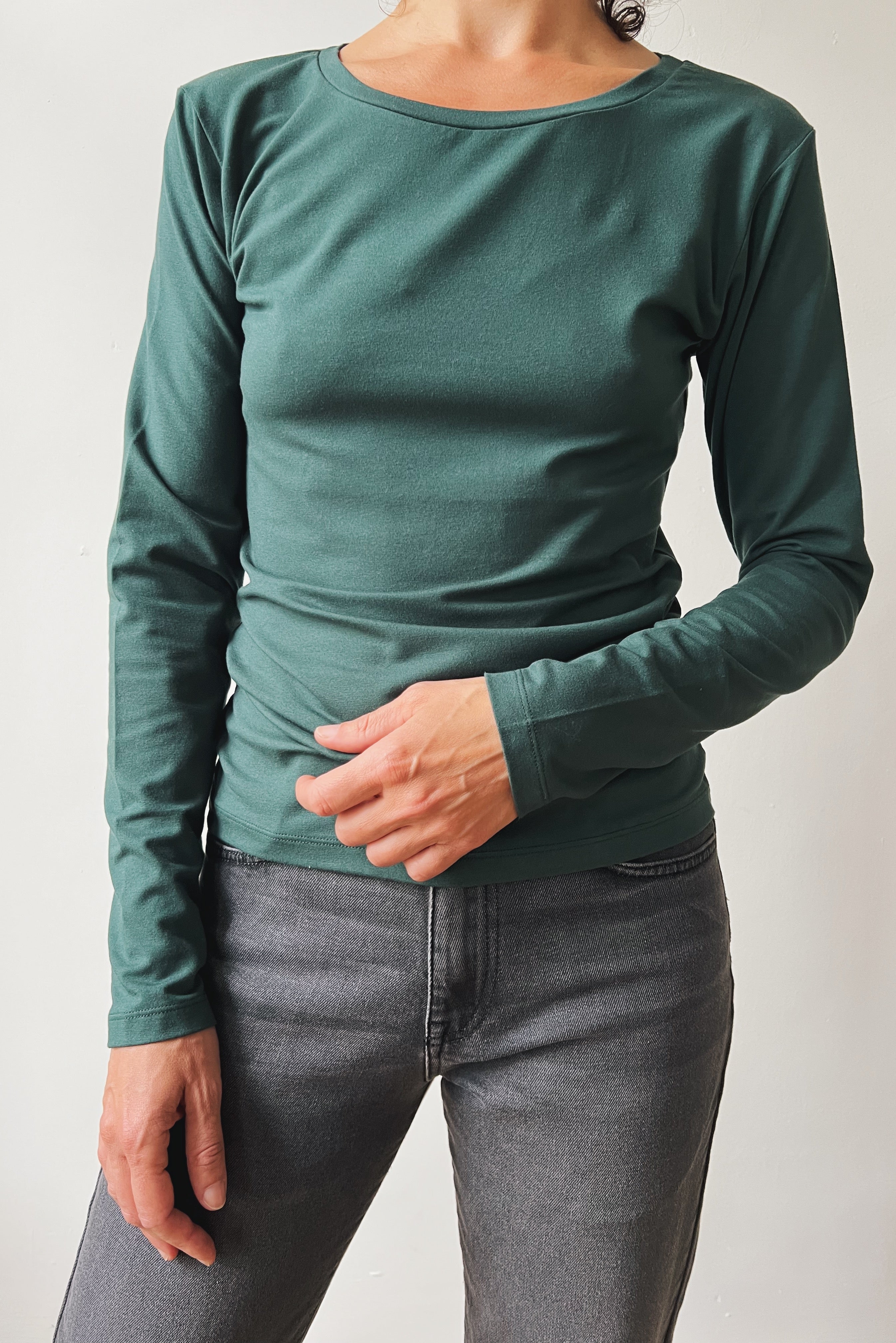 Person wearing a green long-sleeve shirt and gray jeans against a plain background
