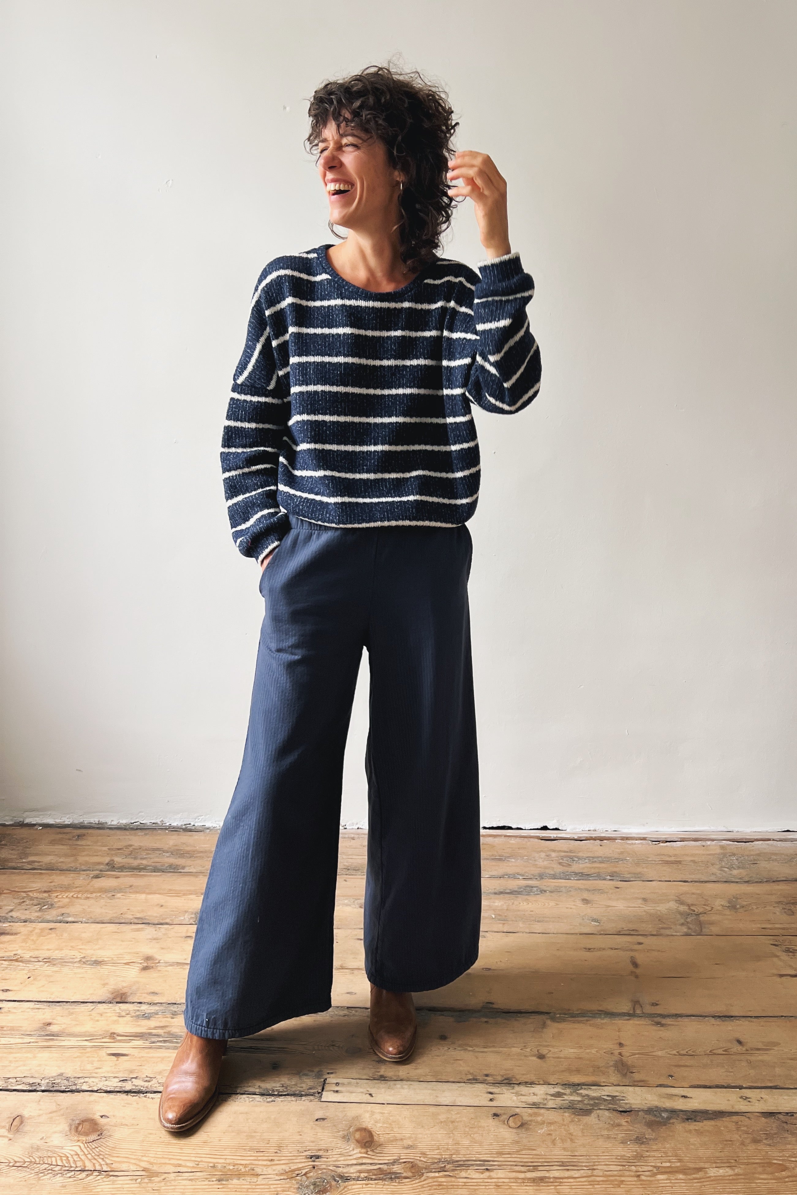Person wearing a striped sweater and wide-leg pants standing on a wooden floor.