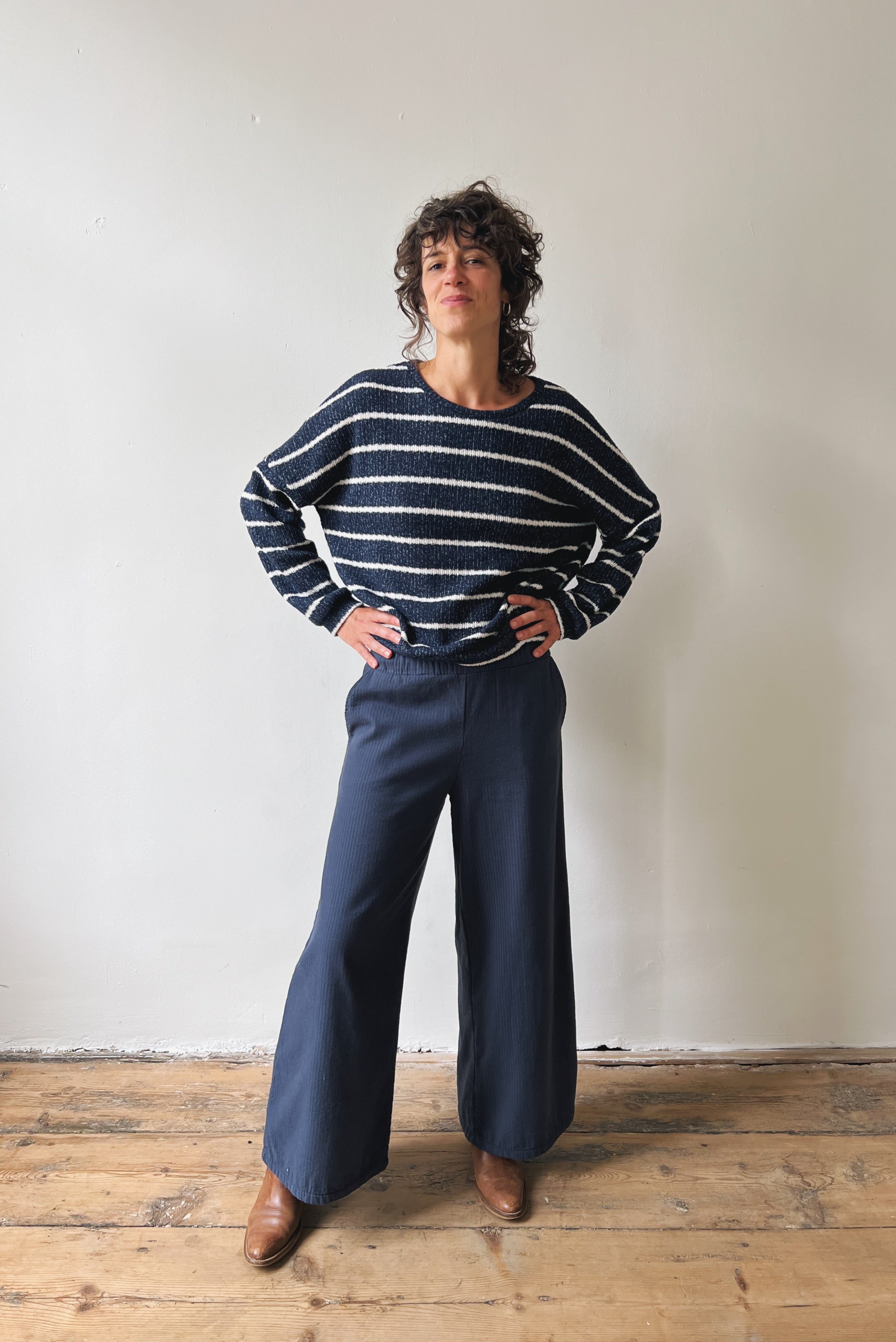 Person wearing a striped sweater and wide-leg pants standing against a plain wall.