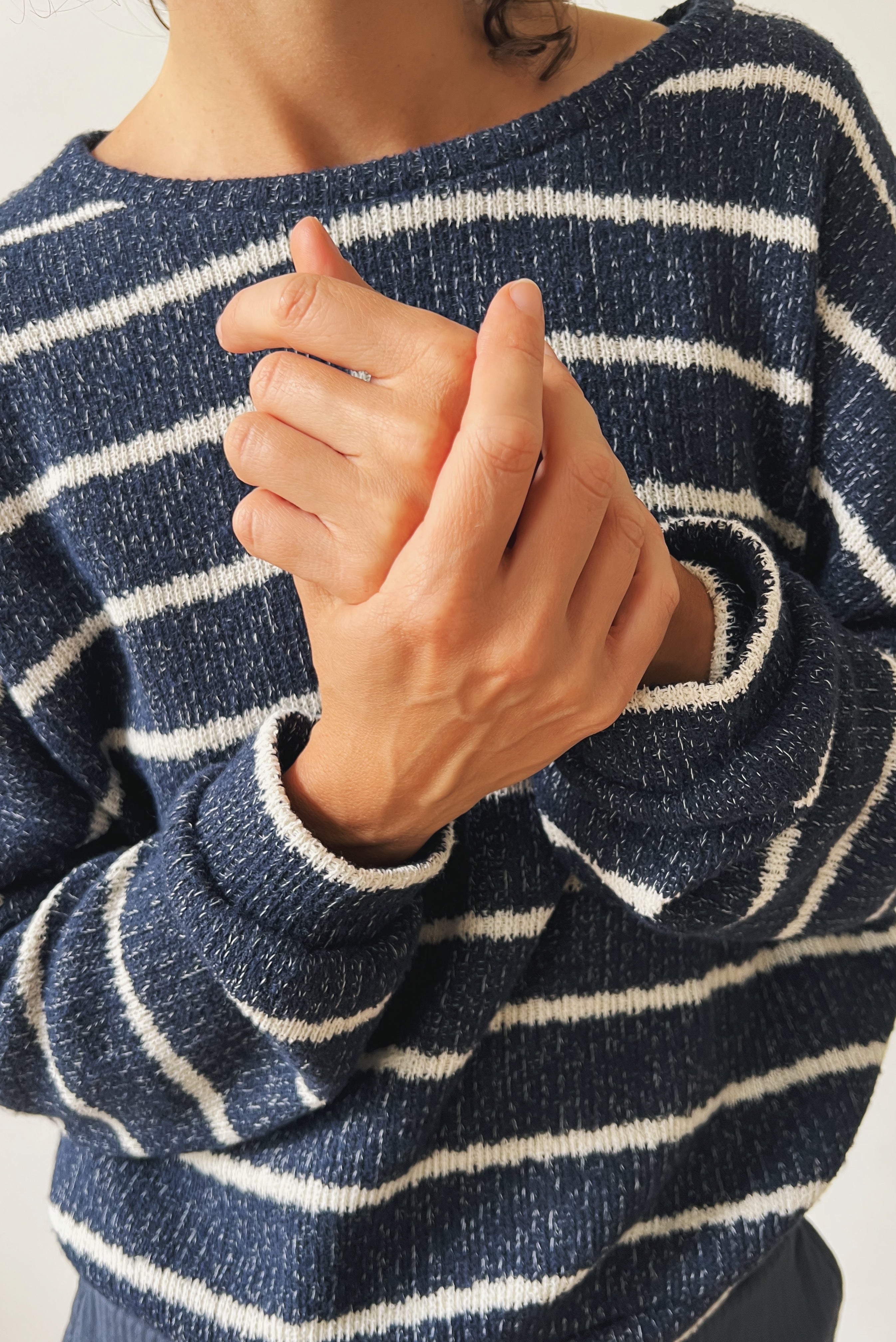 Person wearing a blue and white striped sweater with hands clasped together.