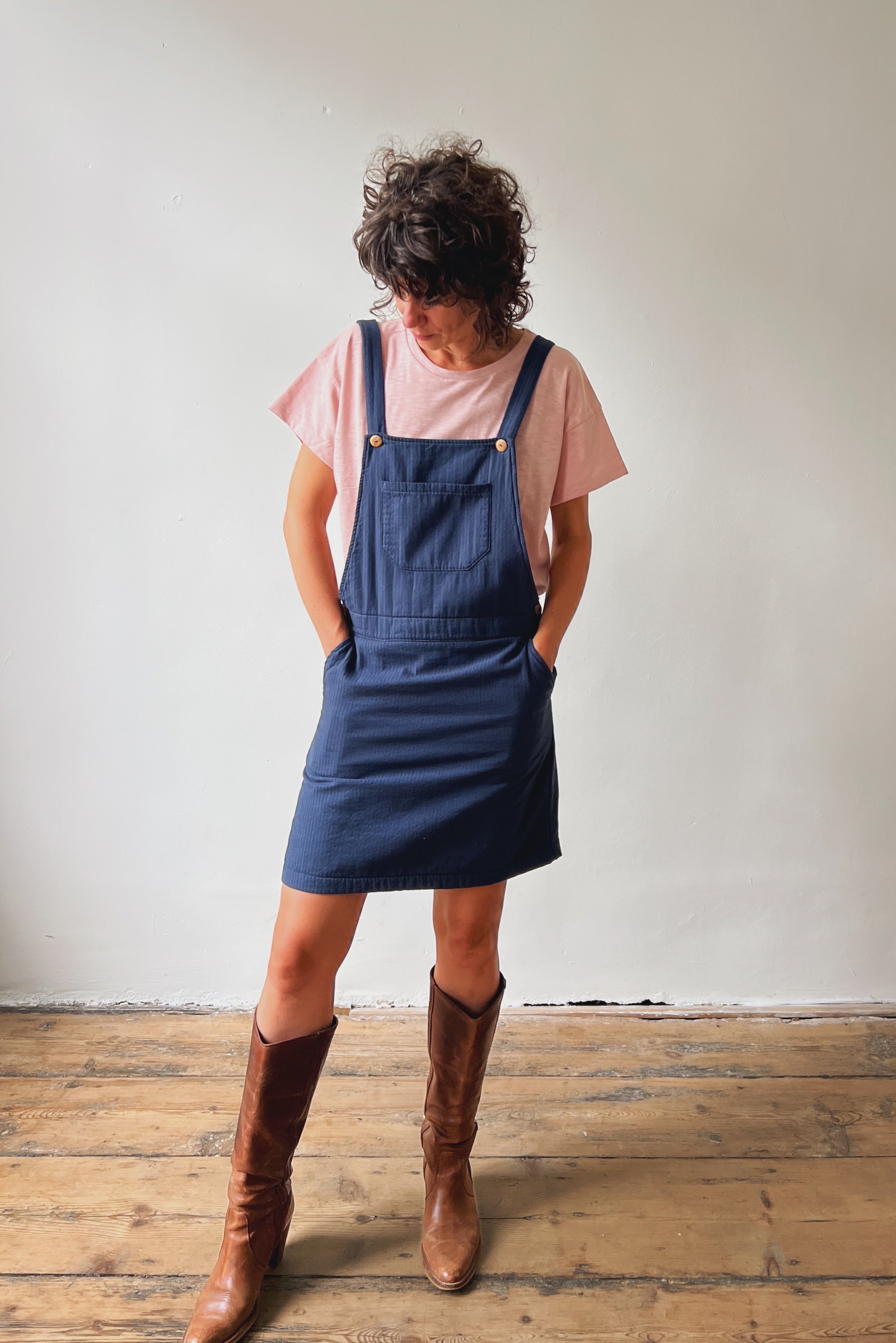 Person wearing a pink t-shirt and blue salopettedress with brown boots