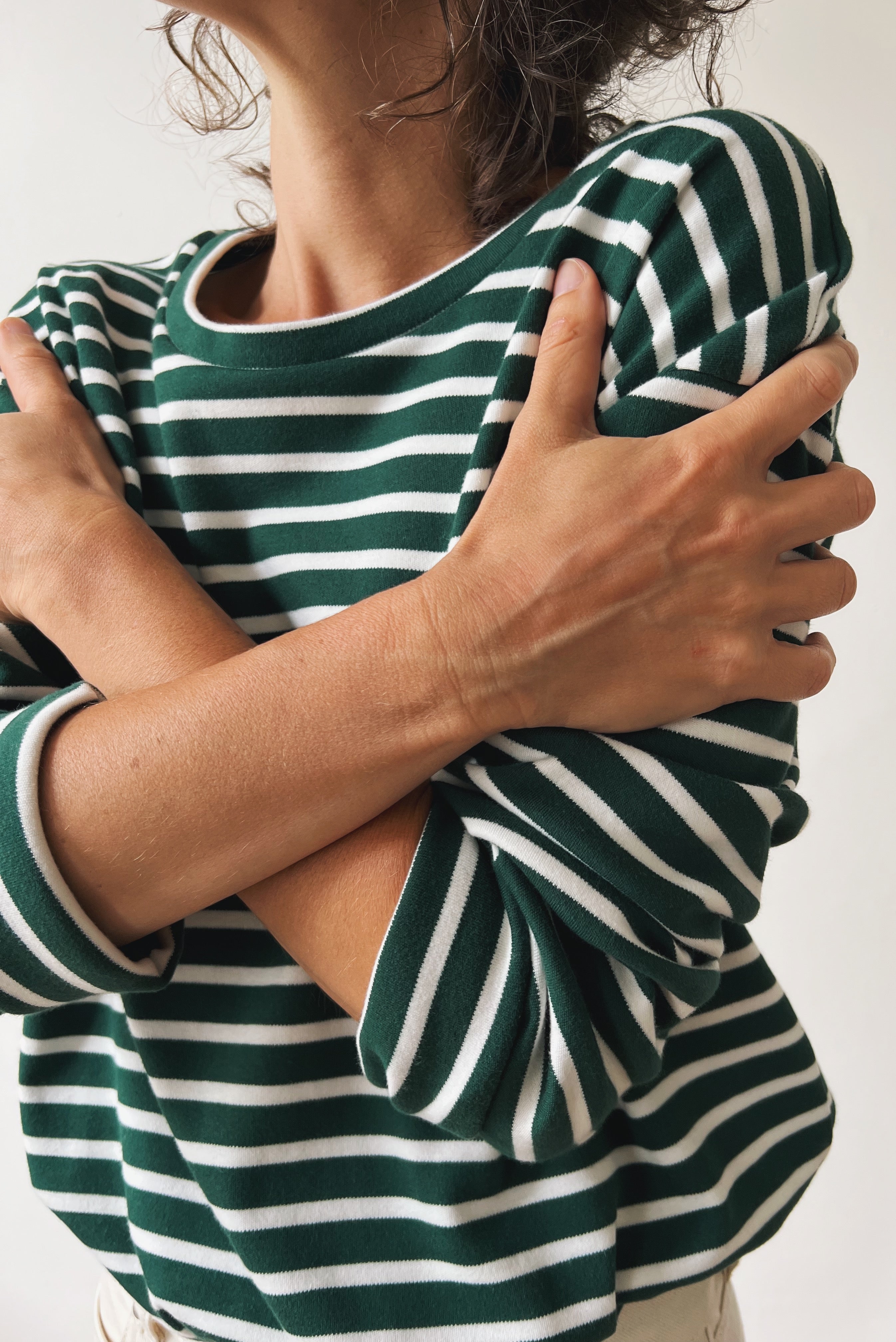 Person wearing a green and white striped shirt with arms crossed.