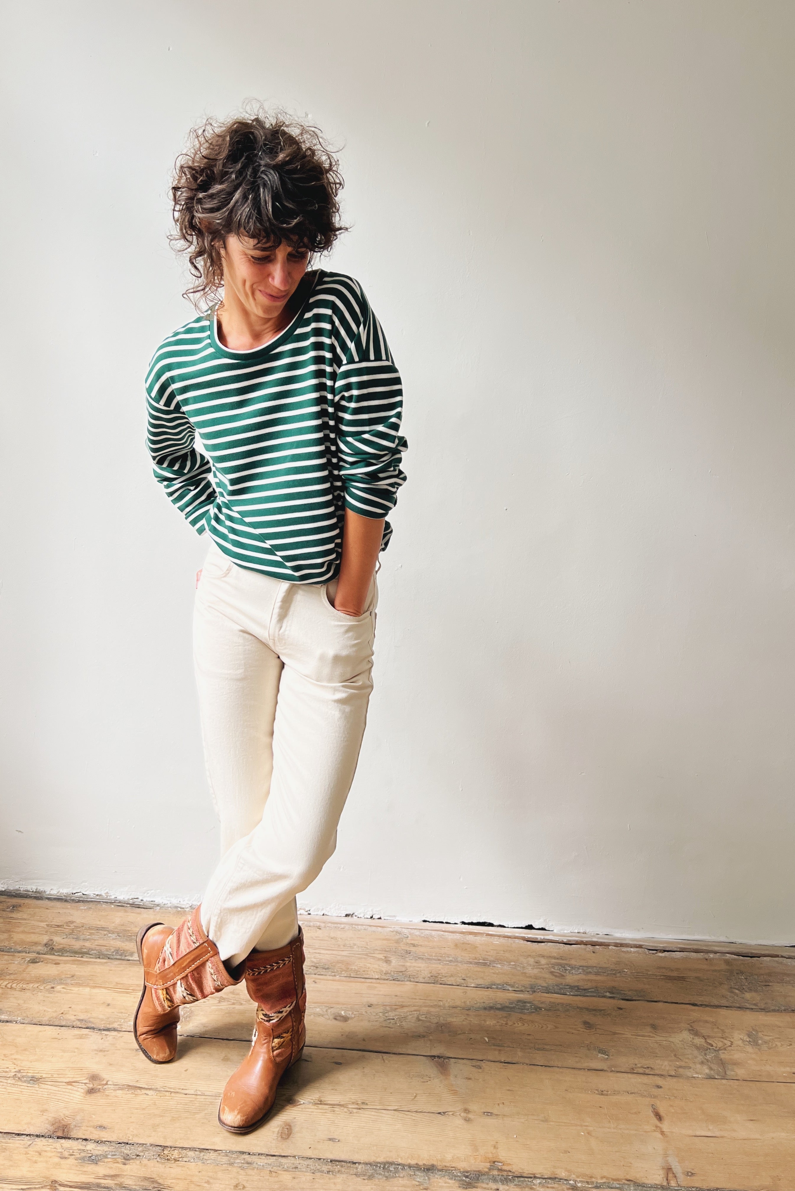 Person wearing a striped sweater, oat jeans, and brown boots against a plain background