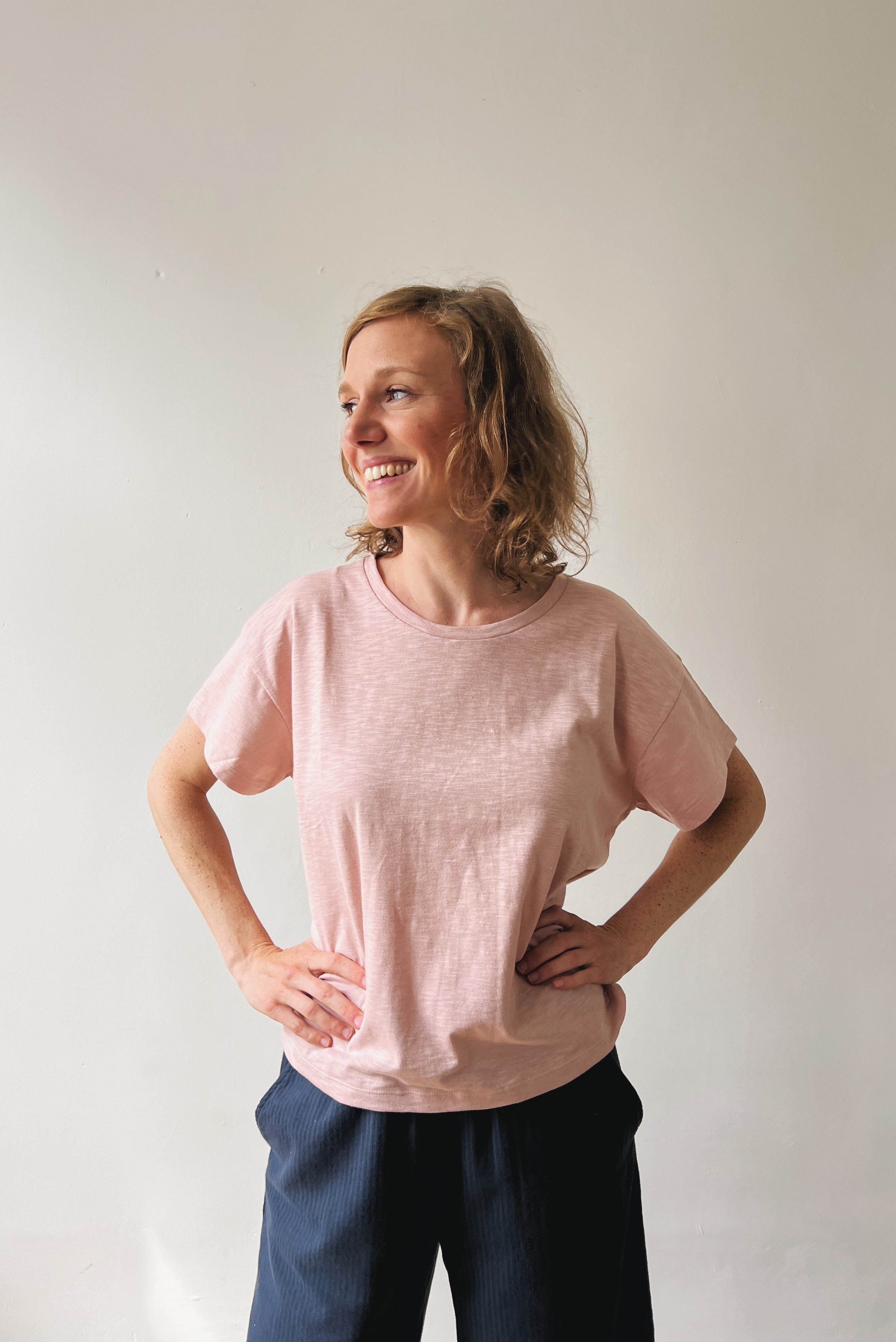 Woman wearing a pink t-shirt and dark pants against a plain background