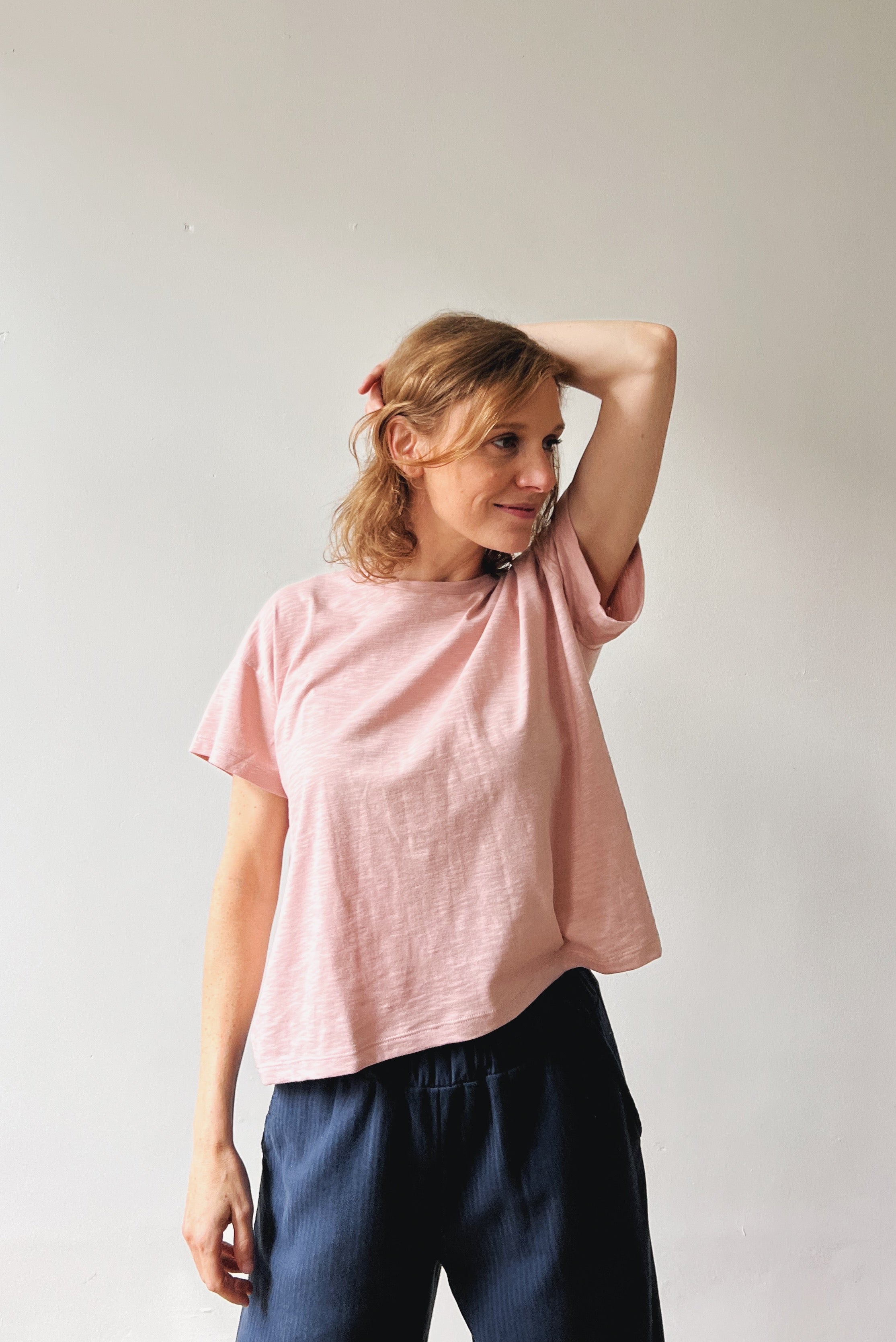 Woman wearing a pink t-shirt and dark pants against a plain background