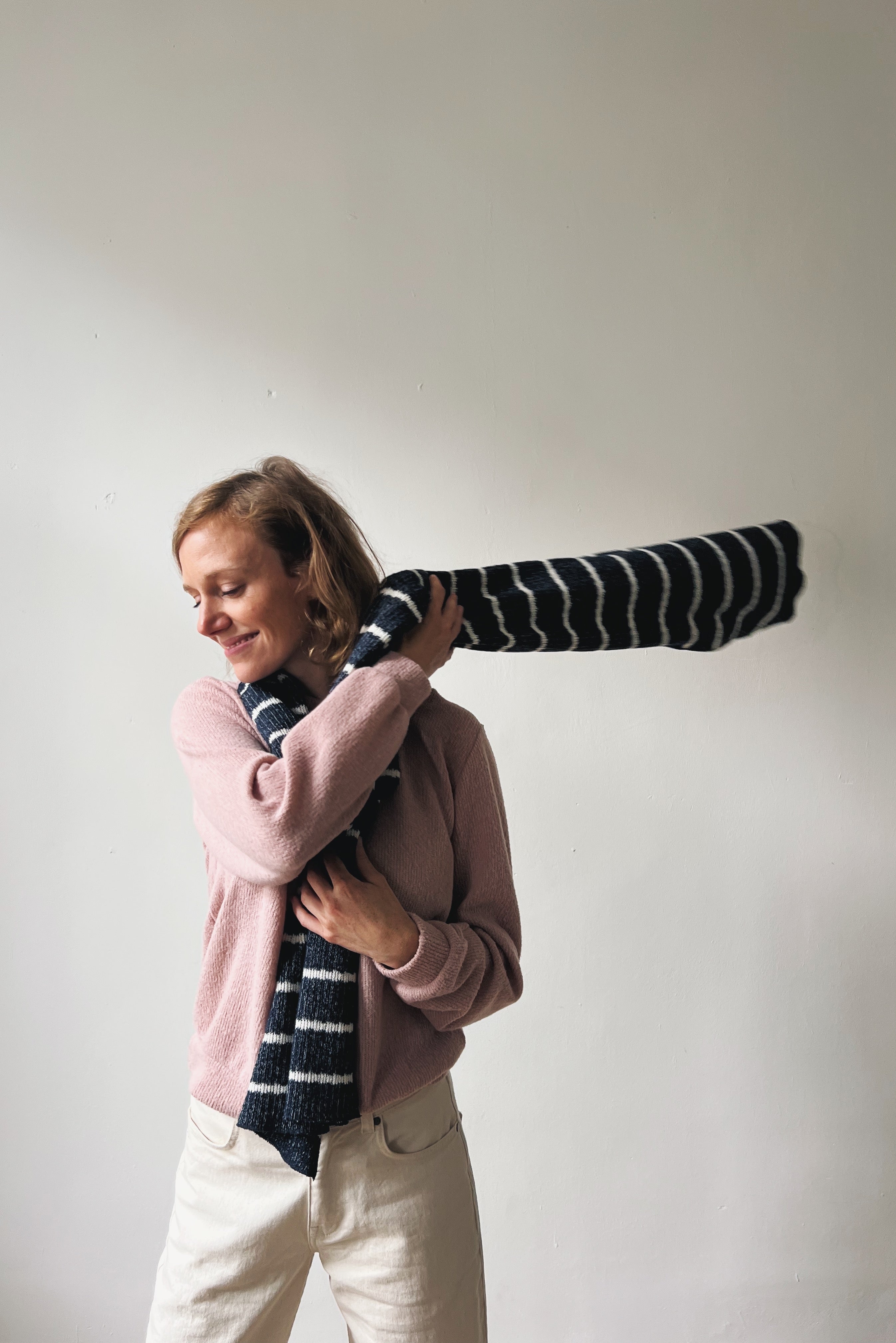 Woman holding a long, striped scarf against a plain background