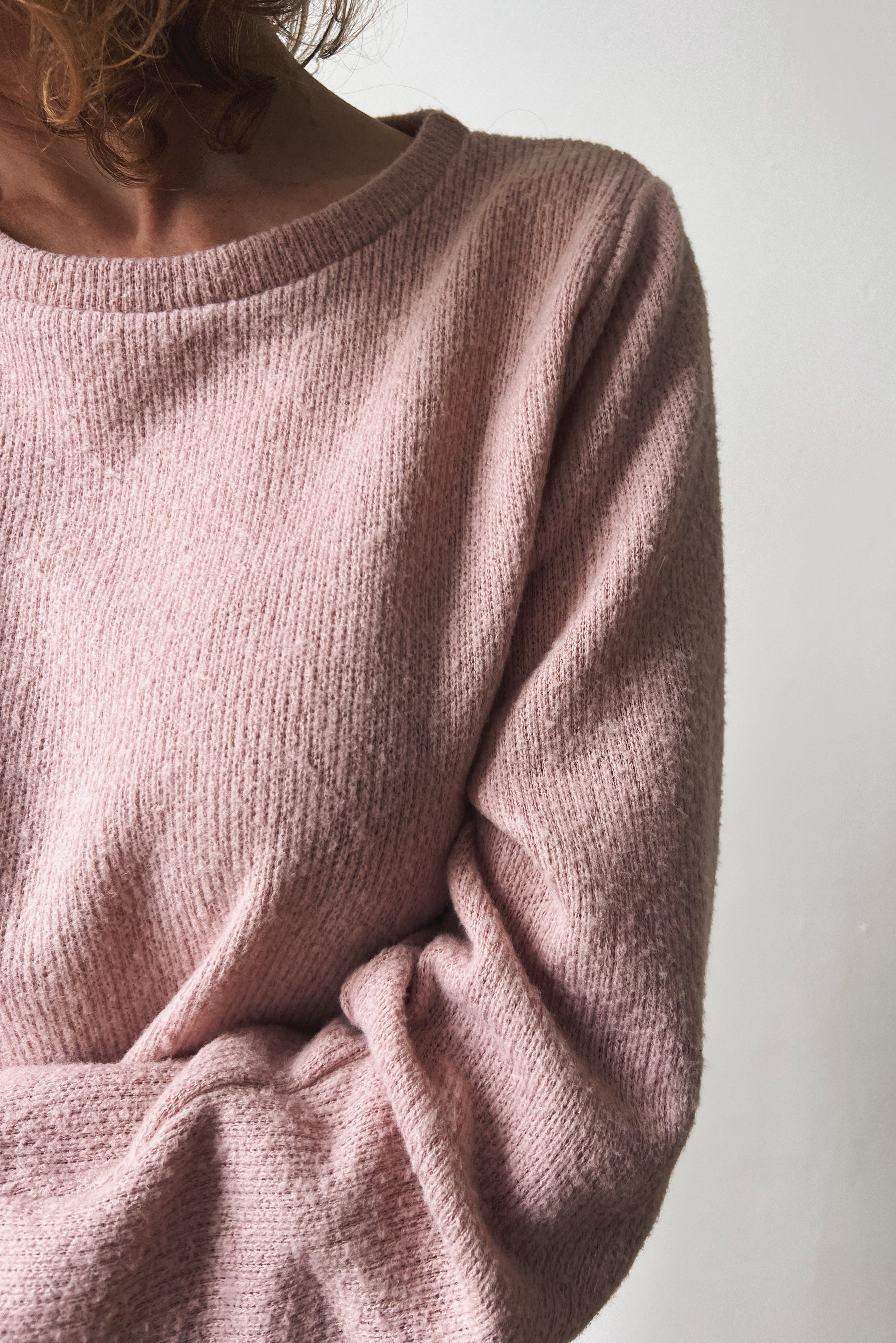 Close-up of a person wearing a pink sweater with a round neckline