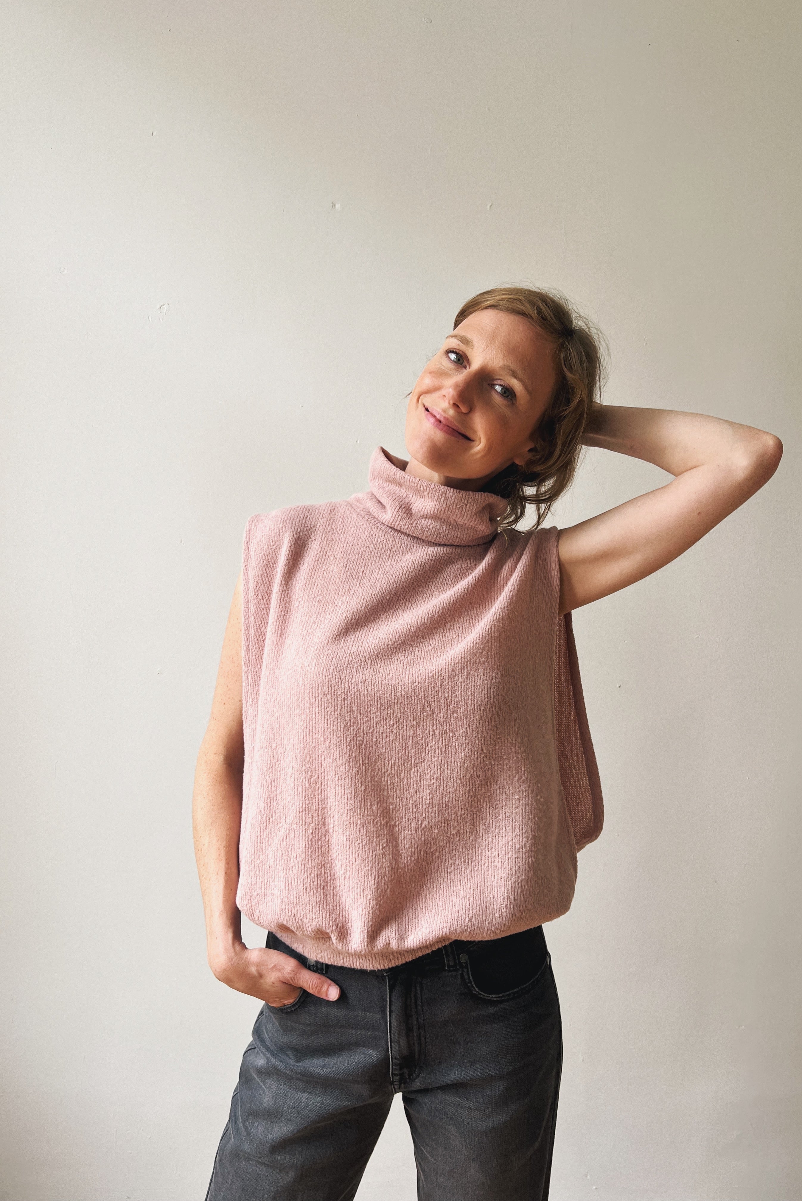 Woman wearing a pink sleeveless sweater against a plain background