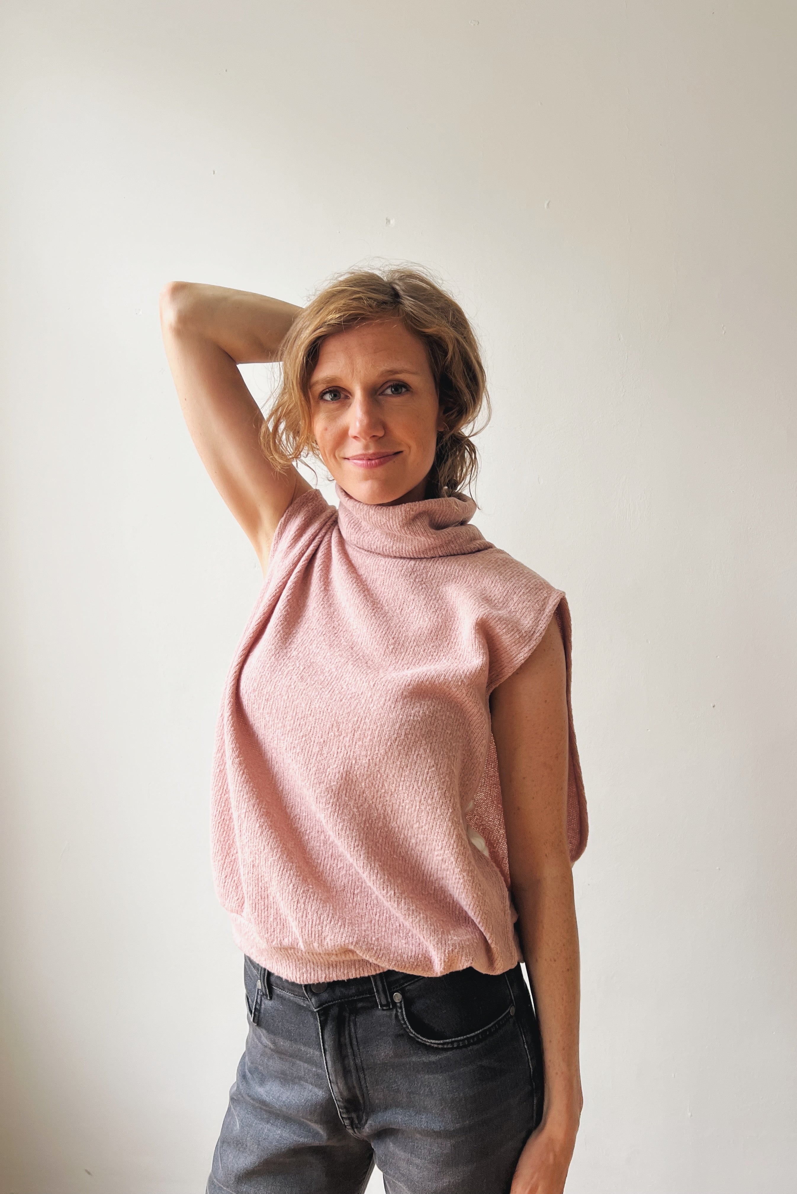 Woman wearing a pink sleeveless sweater and grey boyfriend jeans against a plain background
